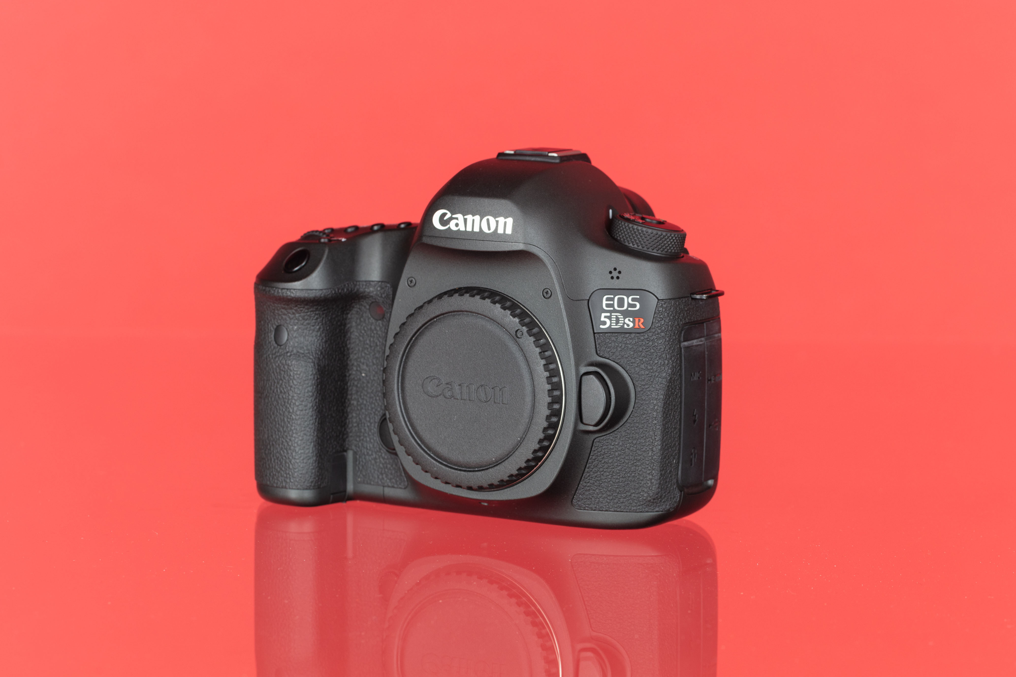 A photo of a Canon EOS 5DS R full-frame DSLR camera against a red background