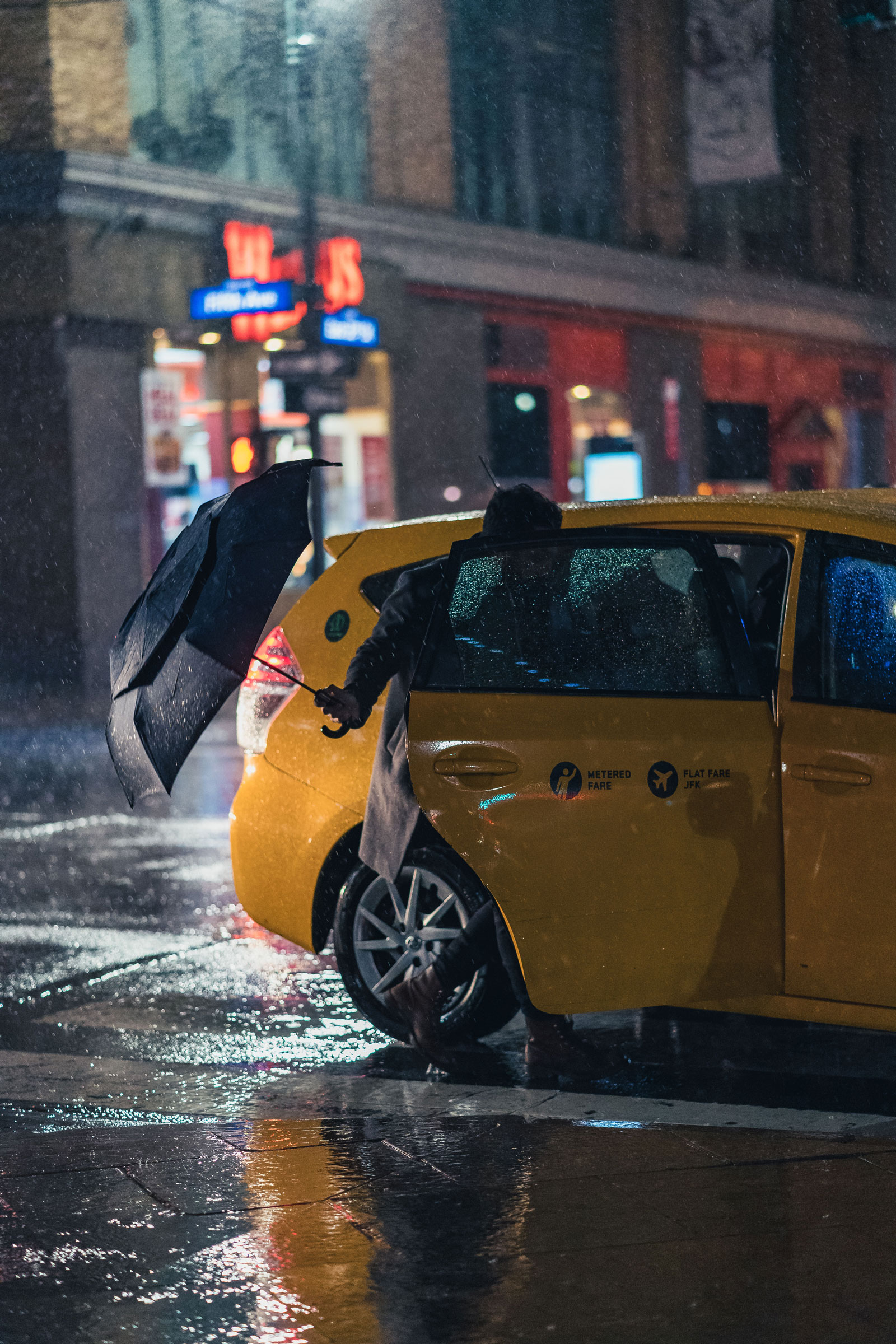 Person getting into taxi cab on rainy night with umbrella in New York City, photo by Manuel Pena on a Sony A7 III.