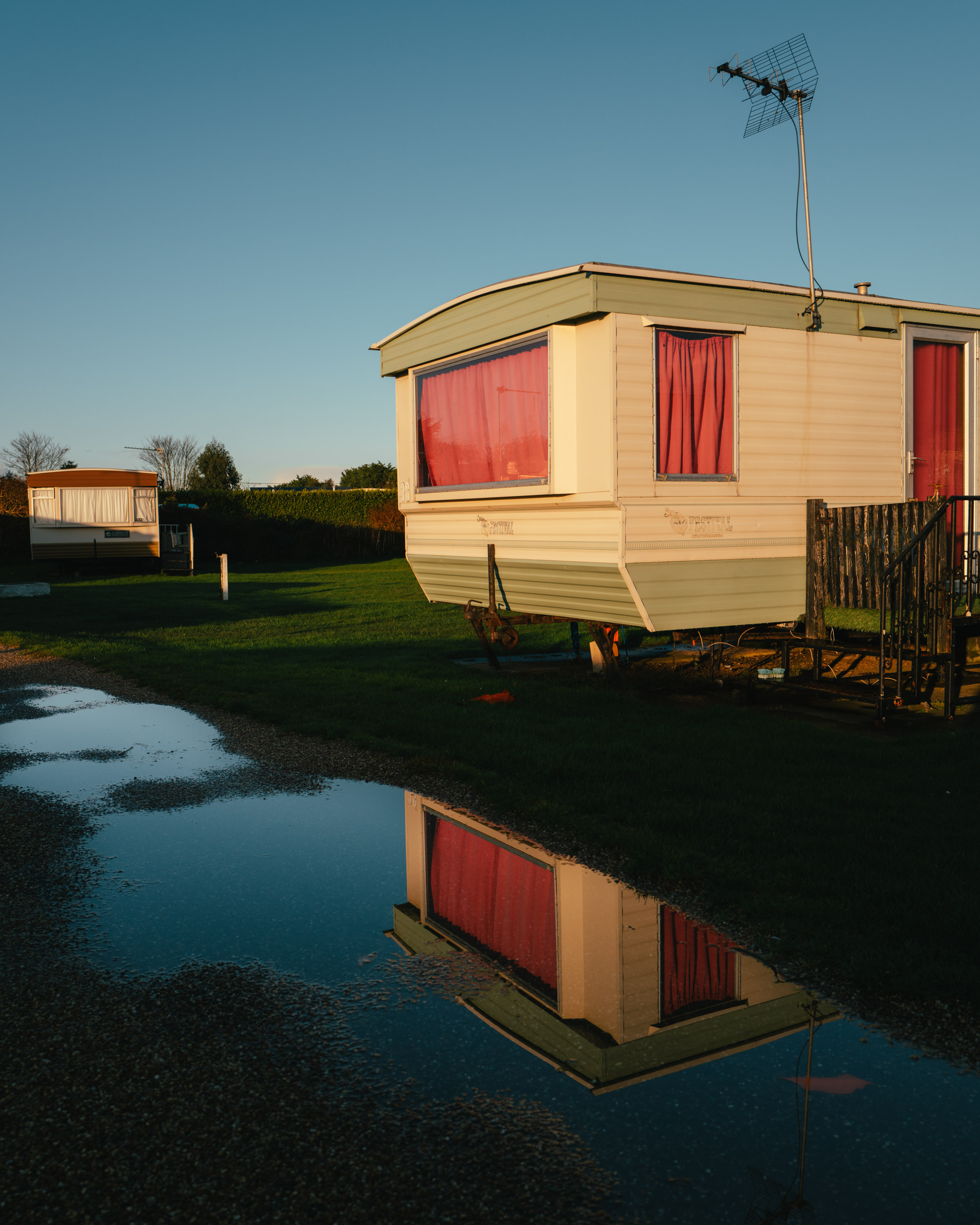 A caravan with pink curtains and a puddle reflecting it on the ground