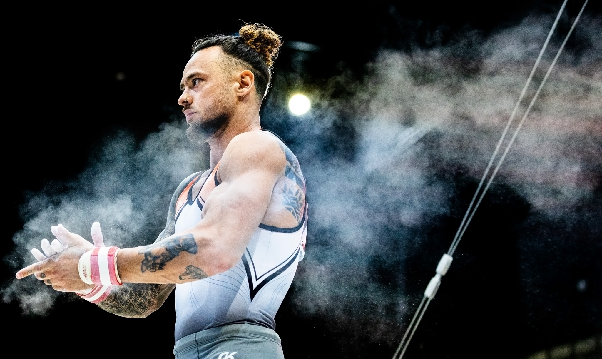 A gymnast dusting their hands together with white chalk for good grip. By Iris van den Broek.