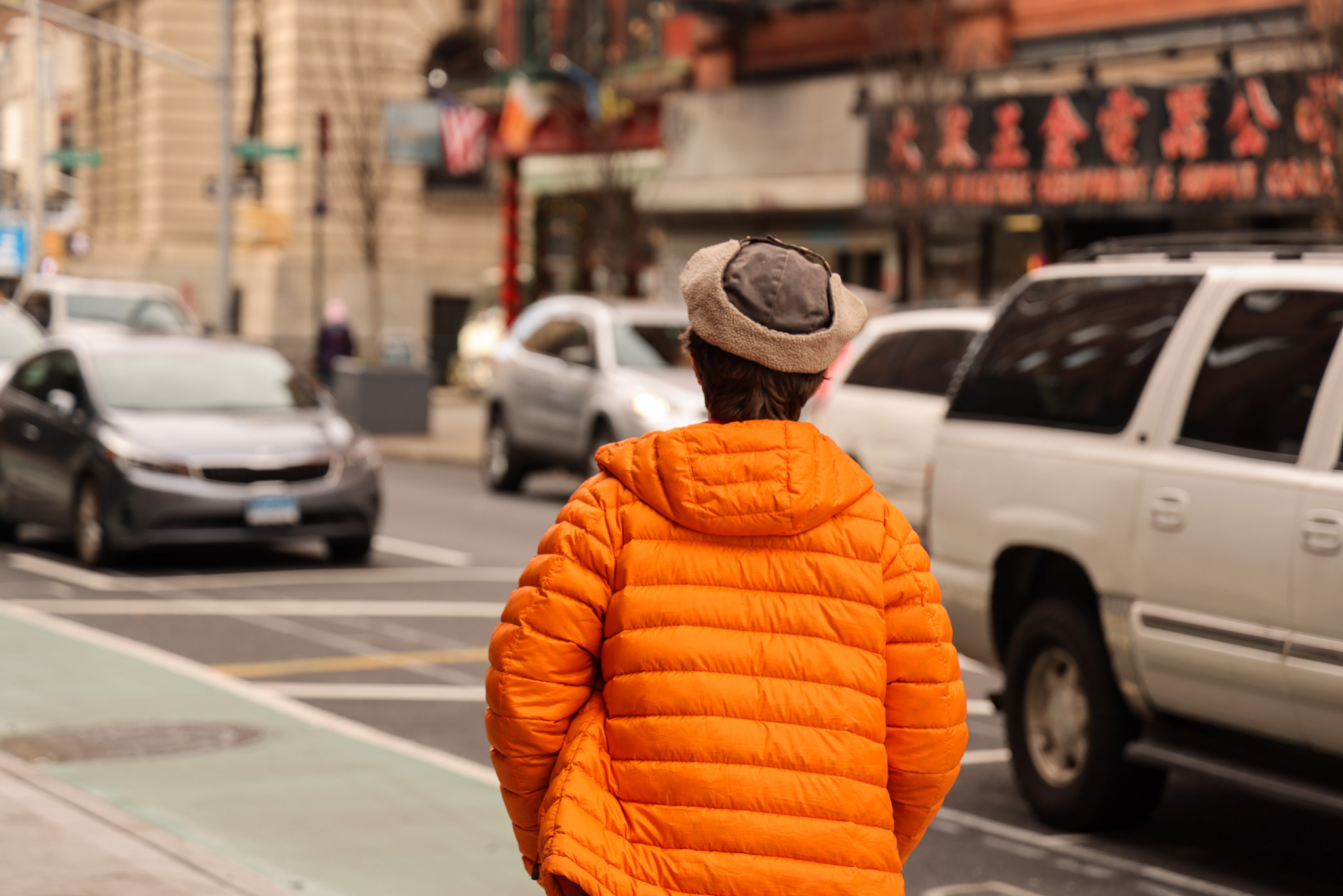 Person walking down the street in New York City’s Chinatown neighbourhood wearing a bright orange coat, photo by Berta Amelinaite.
