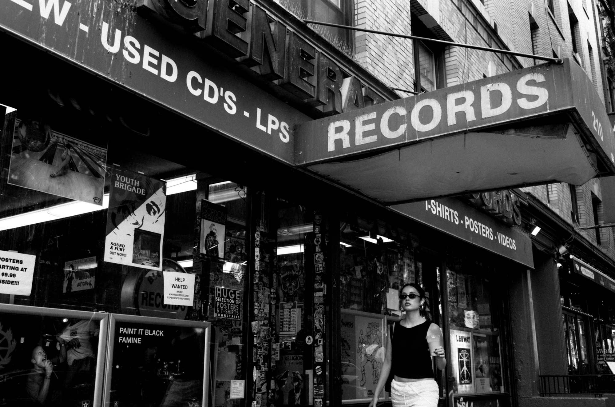 A black-and-white photo of a person walking by a record store