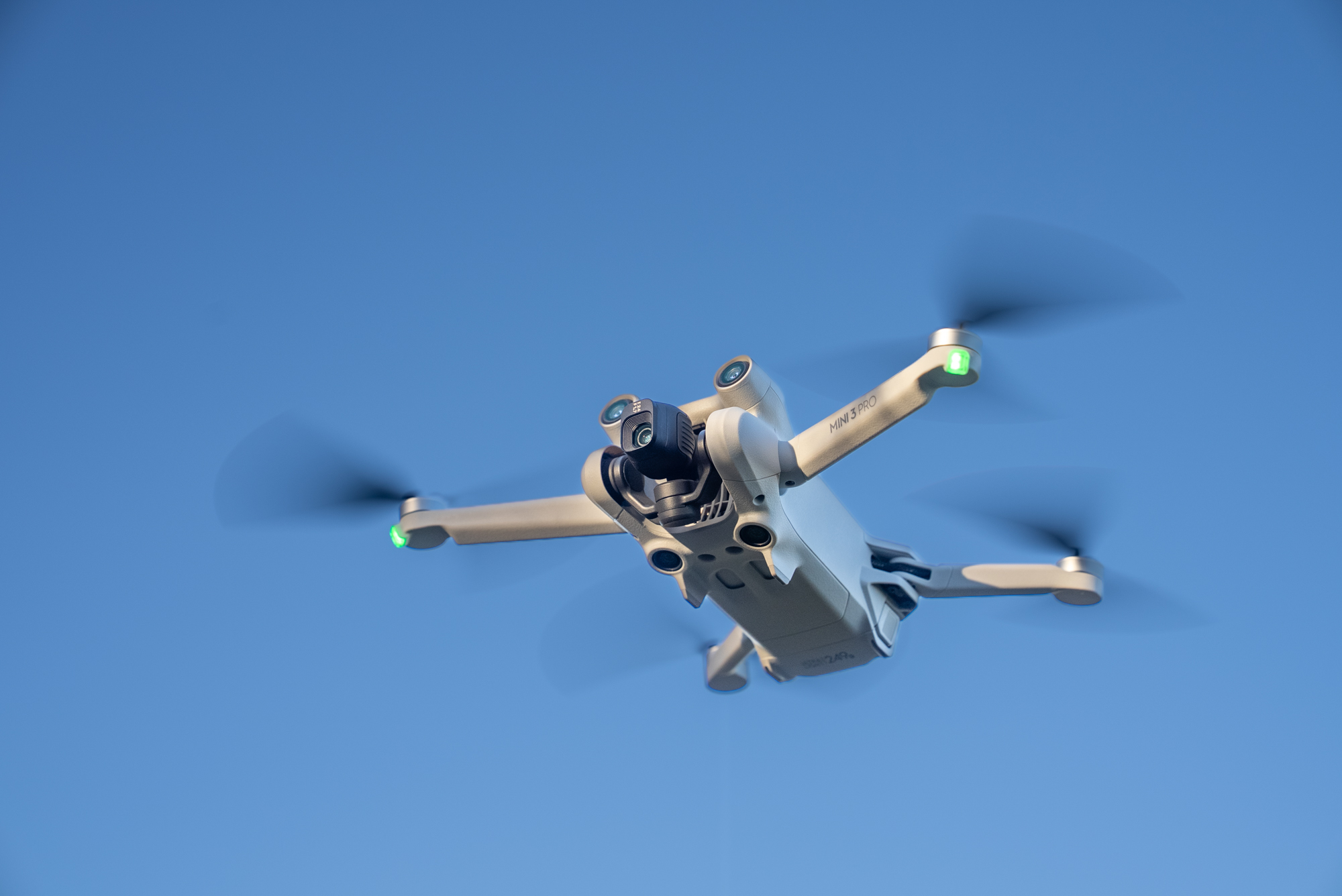 Eine DJI Mini 3 Pro fliegt mit rotierenden Propellern vor einem klaren blauen Himmel. Aufgenommen von Joel Arias mit einer Sony FX3.
