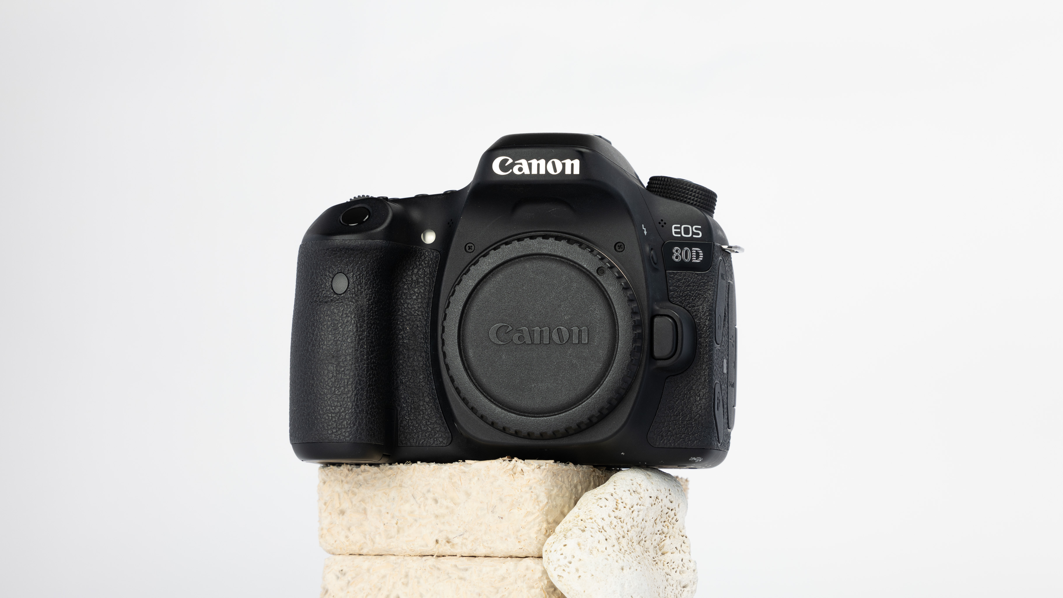 A product shot of a secondhand Canon 80D camera propped up on a rocky podium