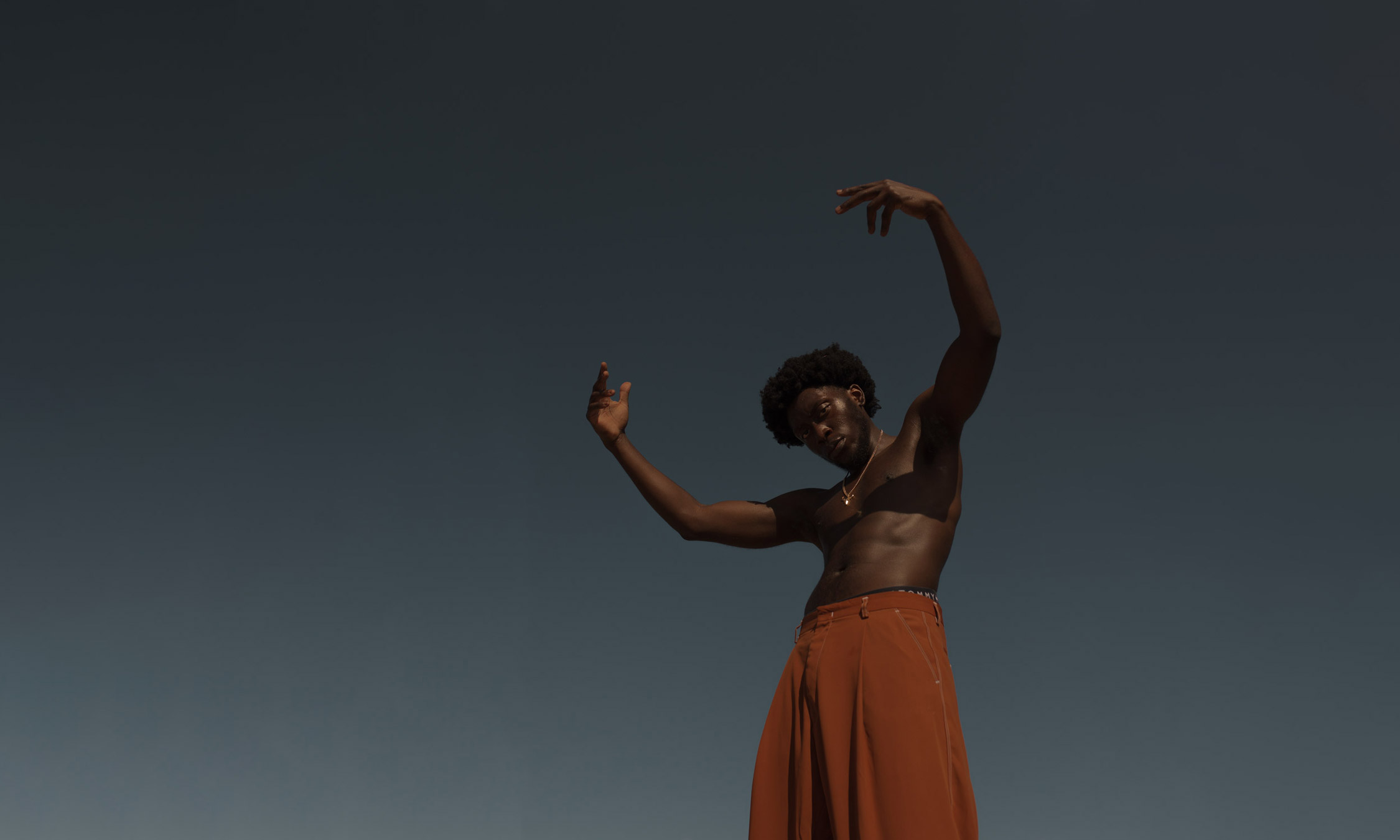 Photo of person wearing orange pants with the sky in the background. Shot by Damola Akintunde.