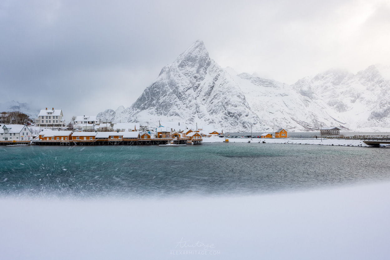 A seaside town sits by a snowy mountain peak.
