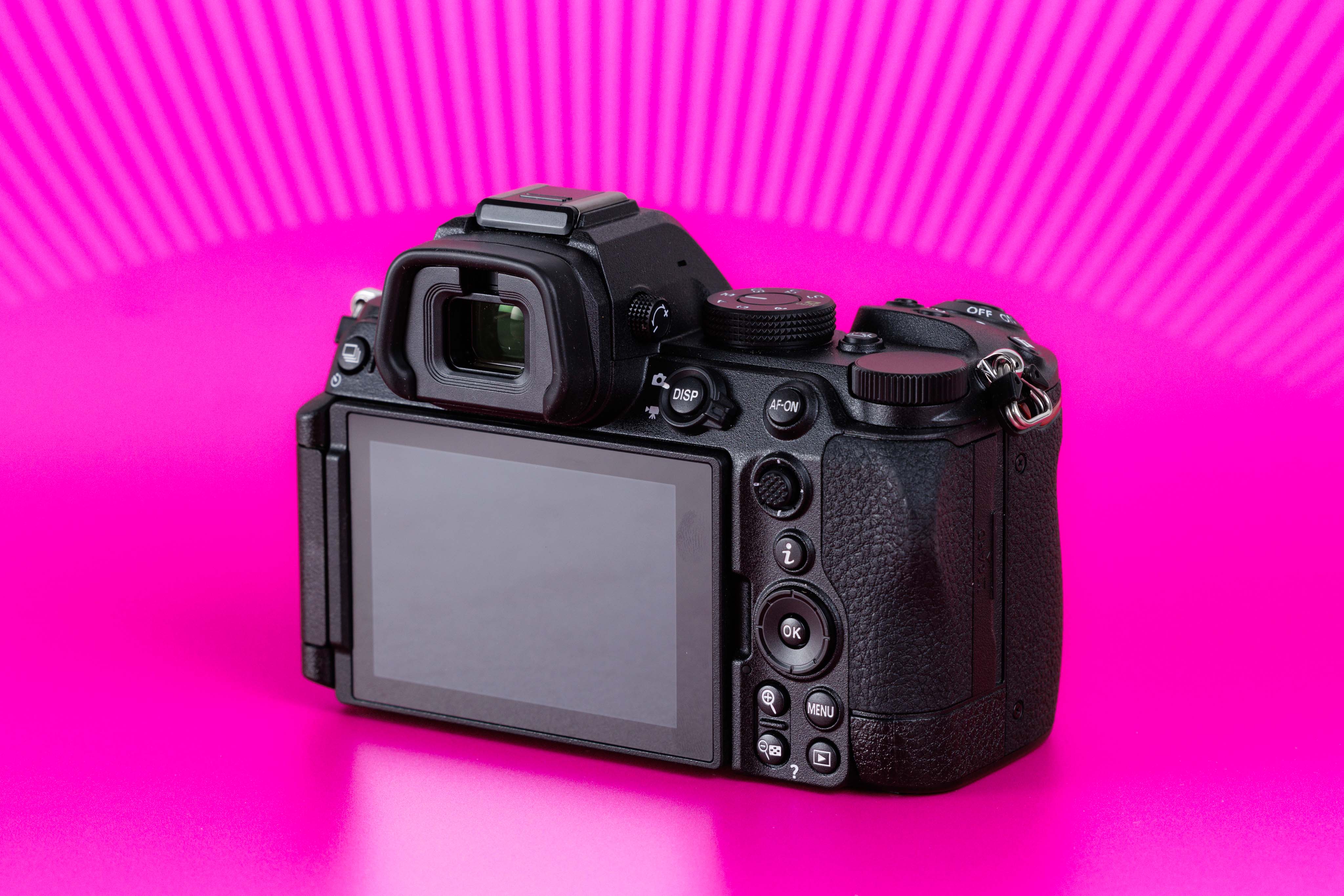 Studioaufnahme der Rückseite einer gebrauchten Nikon Z5 II mit eingeklapptem Display vor leuchtend pinkem Hintergrund