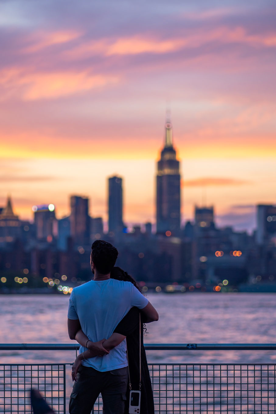 Une photo de deux personnes en train de s'étreindre au bord de l'eau alors que le soleil se couche à New York.