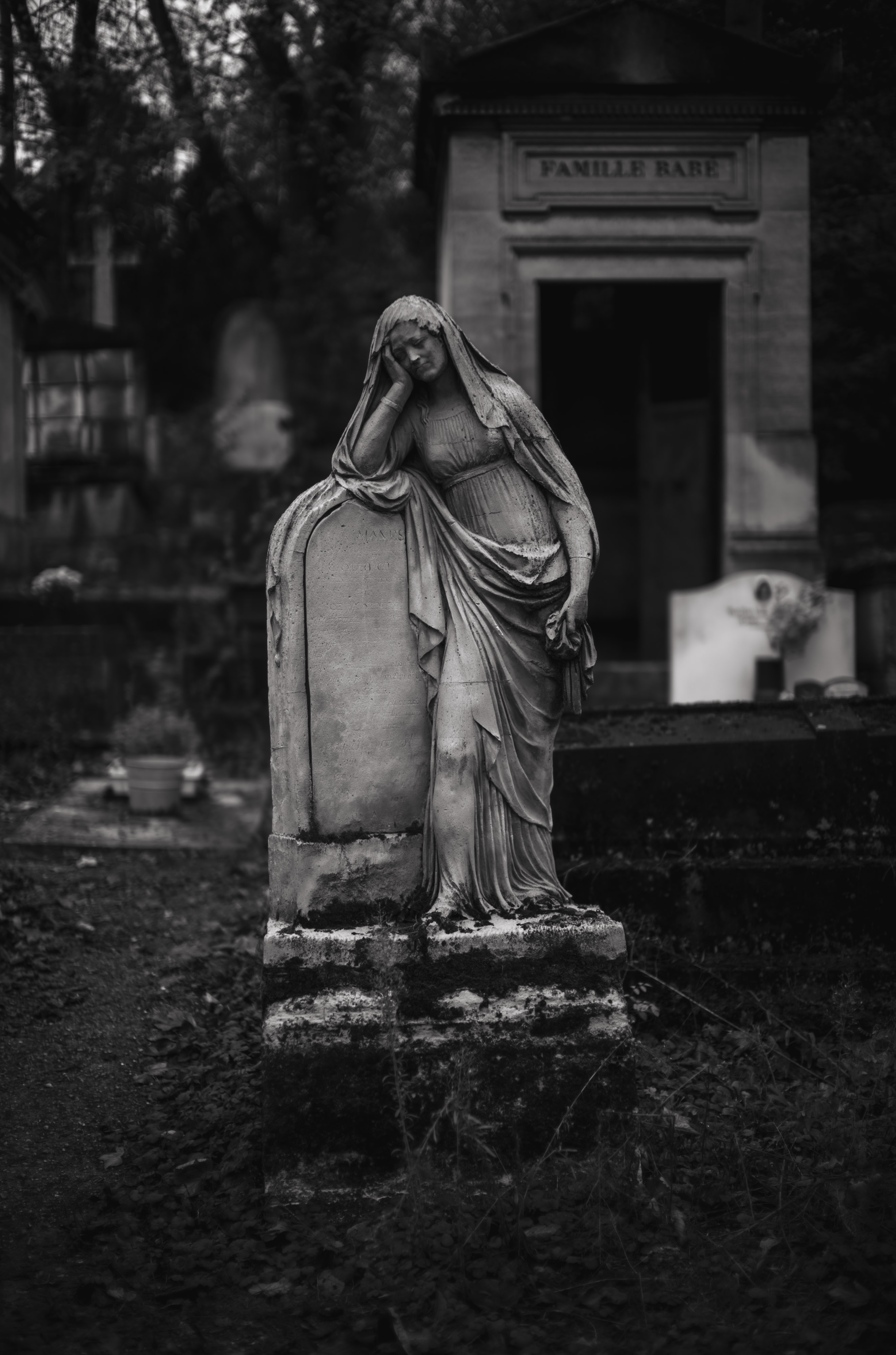 Photo en noir et blanc d'une pierre tombale en marbre blanc devant un mausolée dans un cimetière, prise avec un Leica M10 Monochrom.