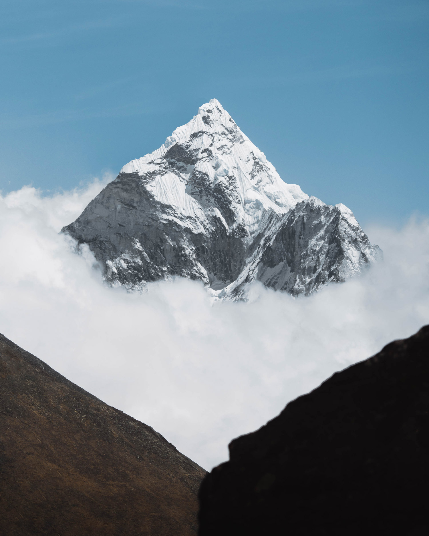 A snow-covered mountain peak pierces white clouds, with two mountain ridges in the foreground, shot by Jack Anstey with the Sony Alpha A7 IV and the Sony FE 70-200mm f/4 G OSS.