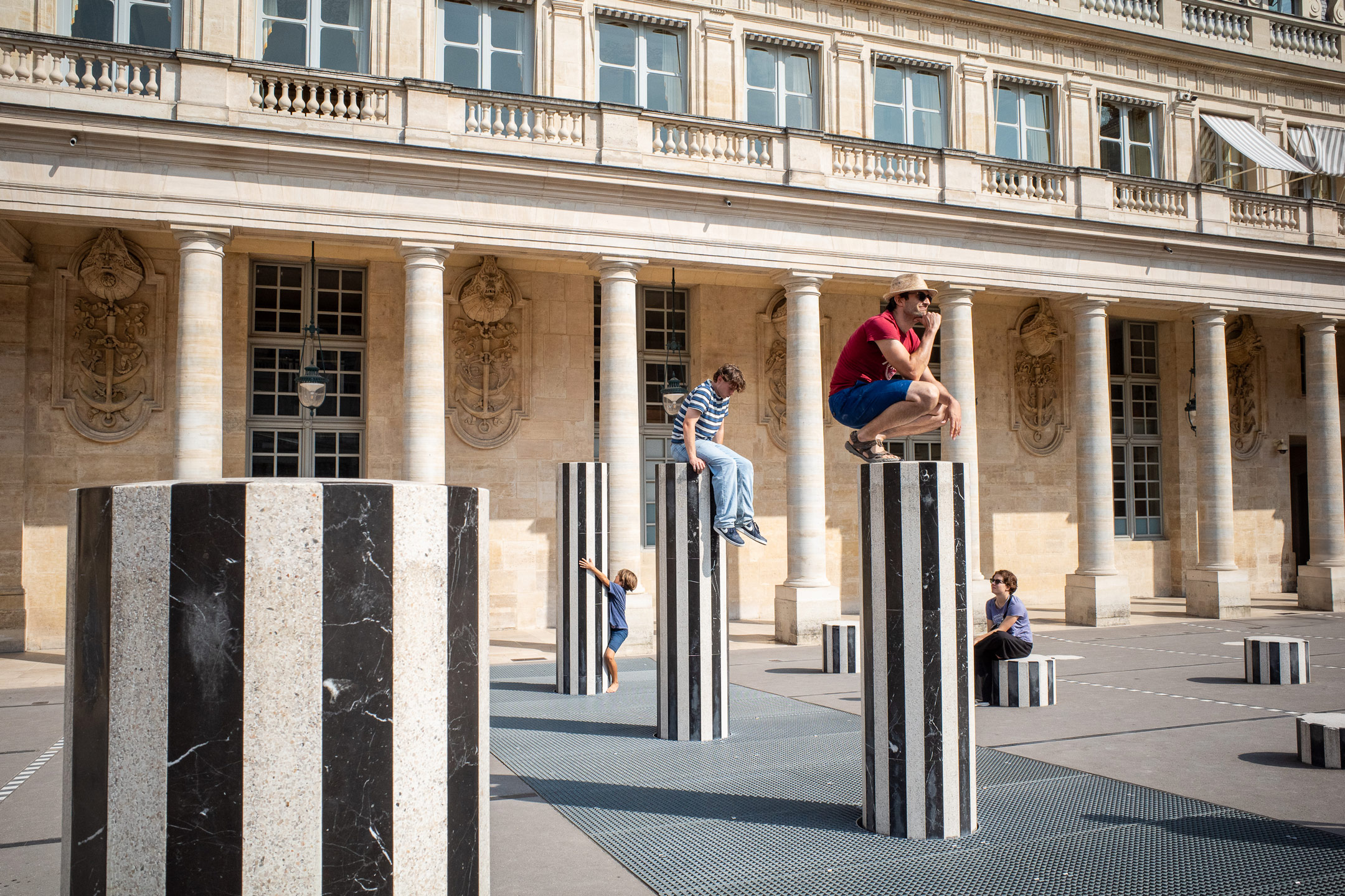 Visitors interact with the black and white striped columns at Palais Royal in Paris, a modern art installation set against historic architecture.