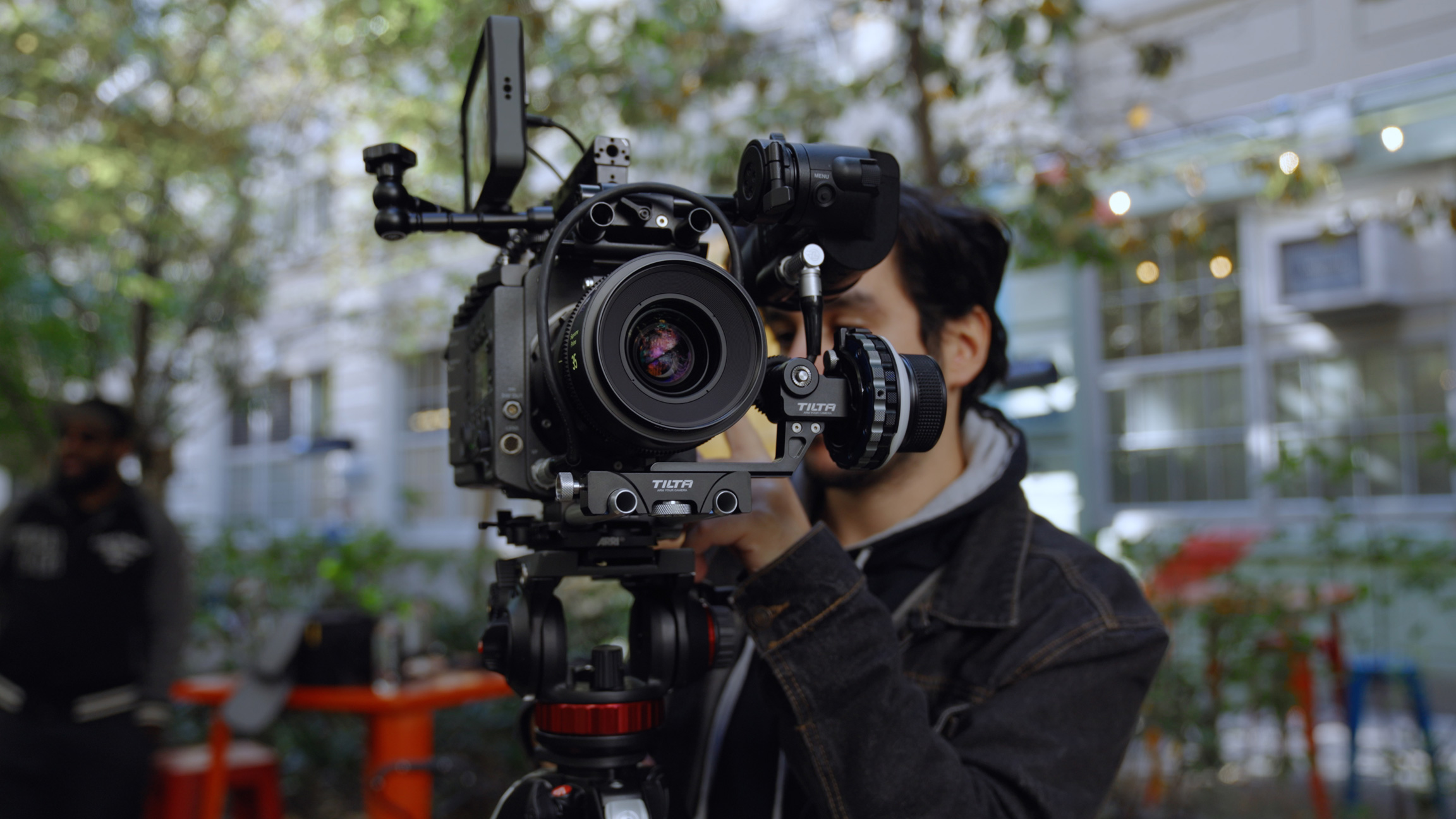 Videographer next to Sony Venice camera on a tripod outside surrounded by trees