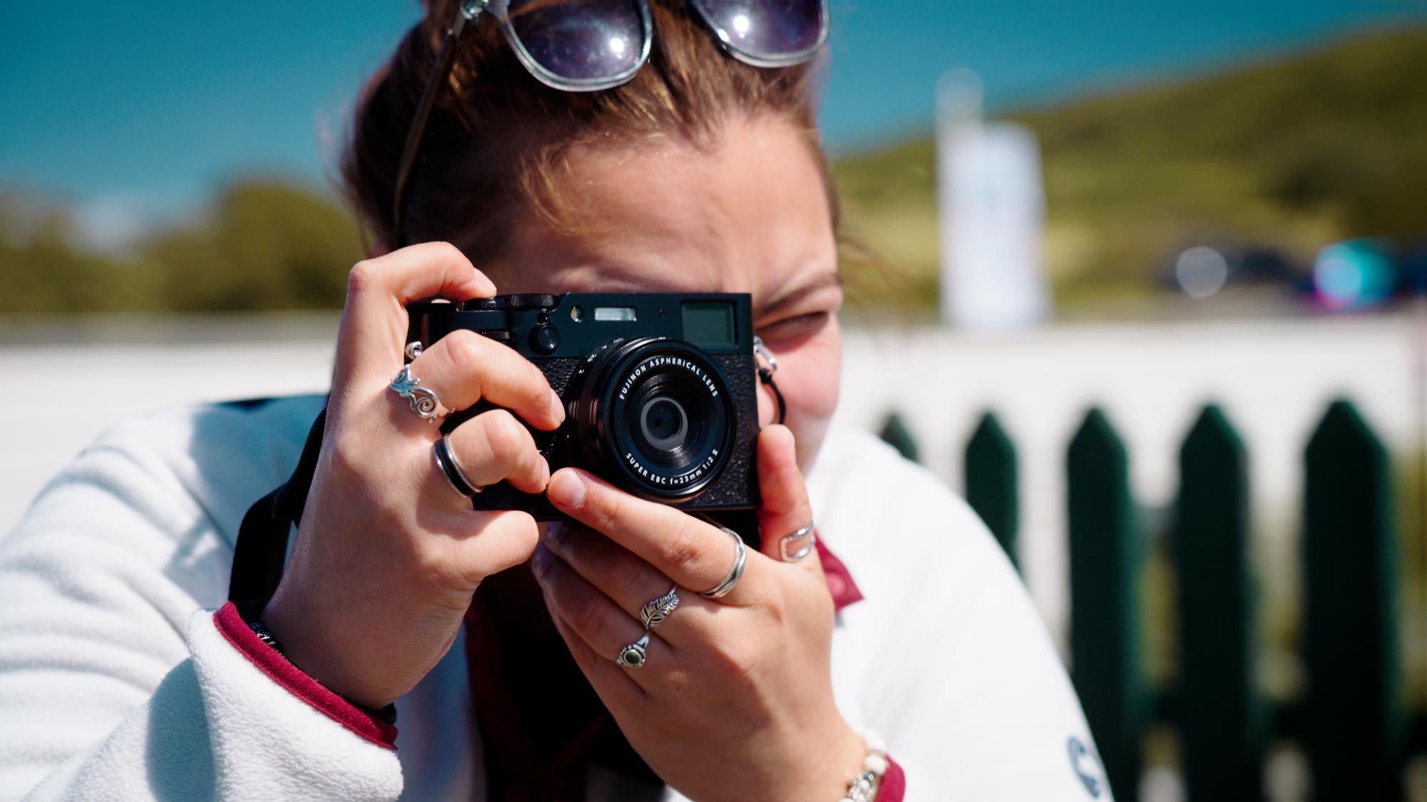 Amy holds a used Fujifilm X100VI up to her eye as she shoots a photo in the sun on the Isle of Wight.