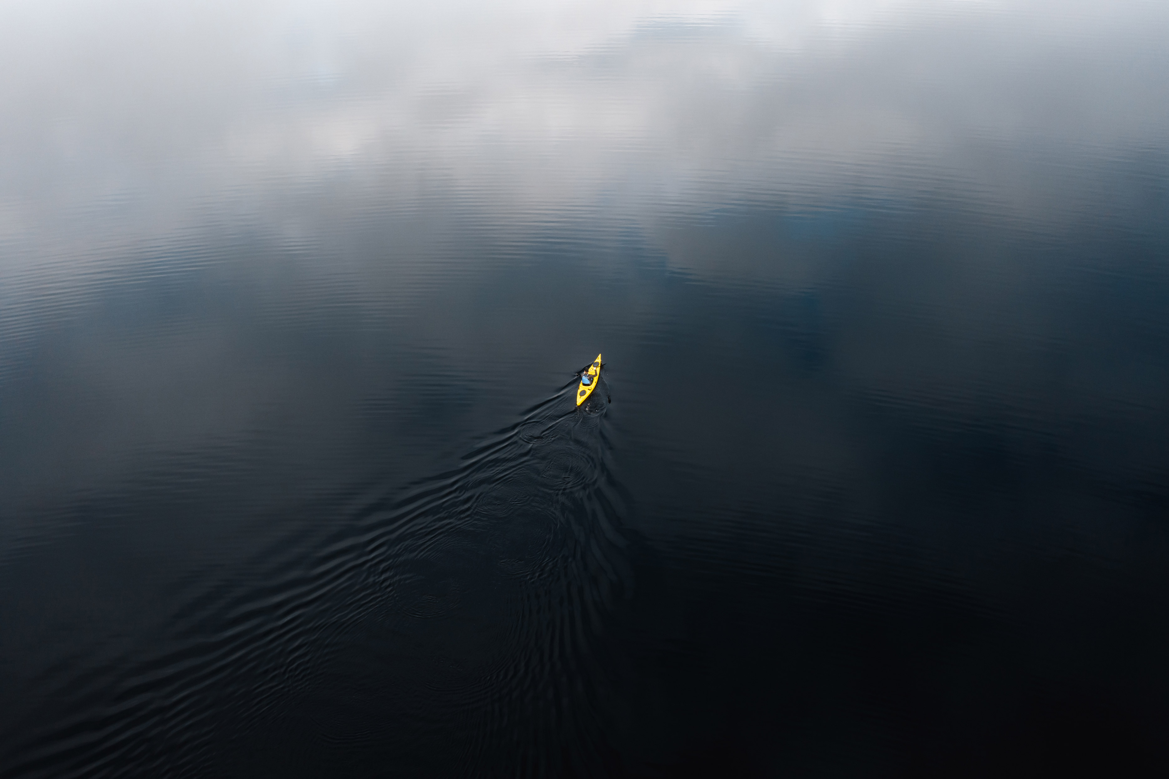 A yellow kayak, photographed from above at a great distance, surrounded by dark water, shot by Jonas Hanspach with a DJI Mavic Air 2S

