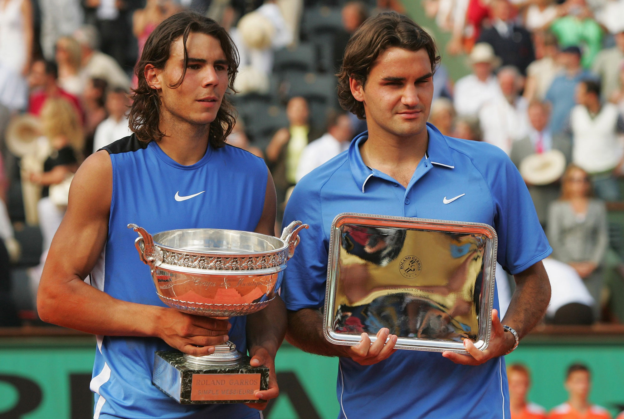 Rafael Nadal (L) of Spain looks on after defeating Roger Federer (R) of Switzerland during the Men's Singles Final of the French Open in Paris, France. The two stand side by side with their respective trophies, with the crowd blurred in the background.