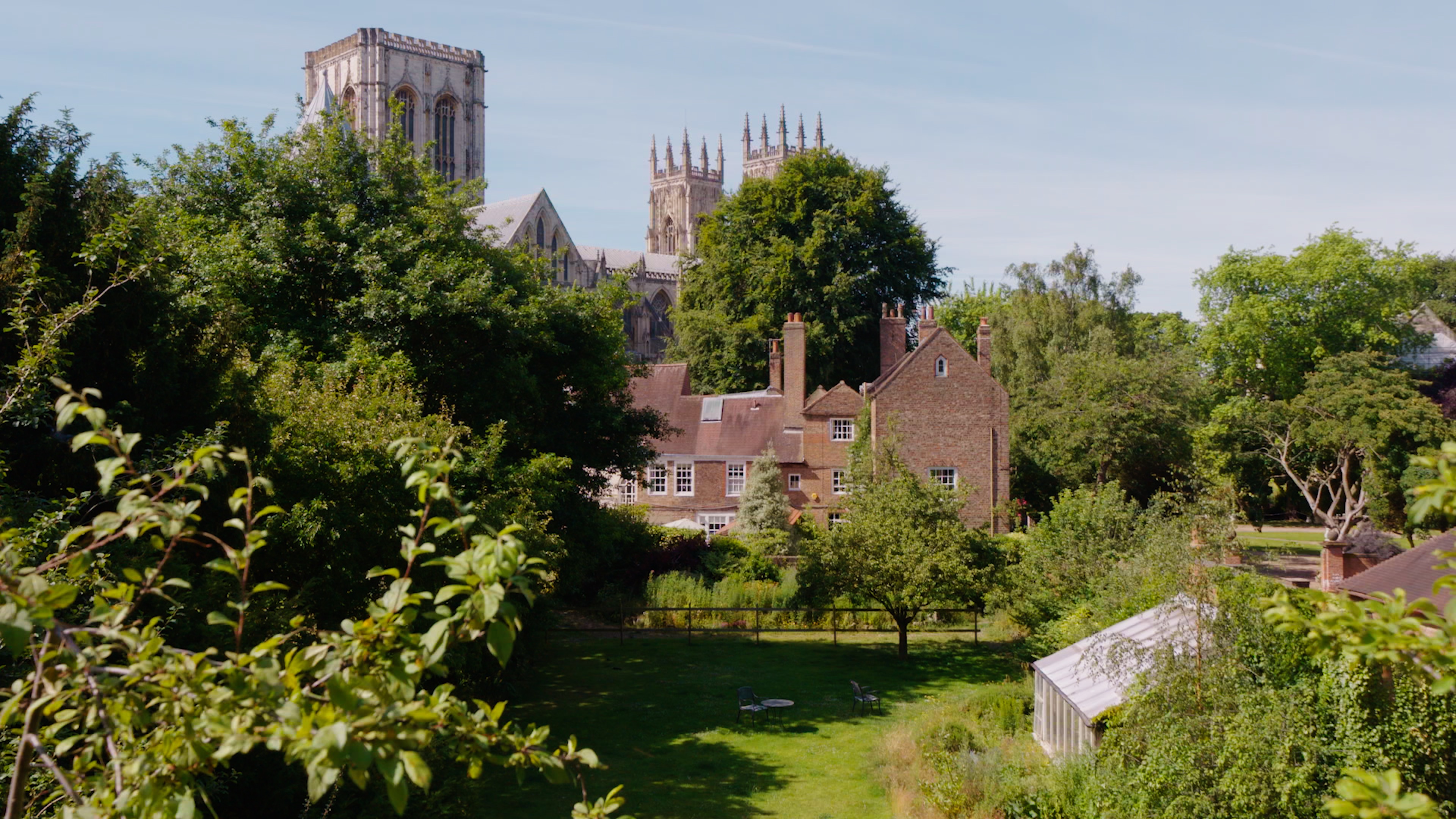Vue sur un jardin verdoyant, une serre, des maisons en briques et la cathédrale de York qui se profile à l'horizon.
