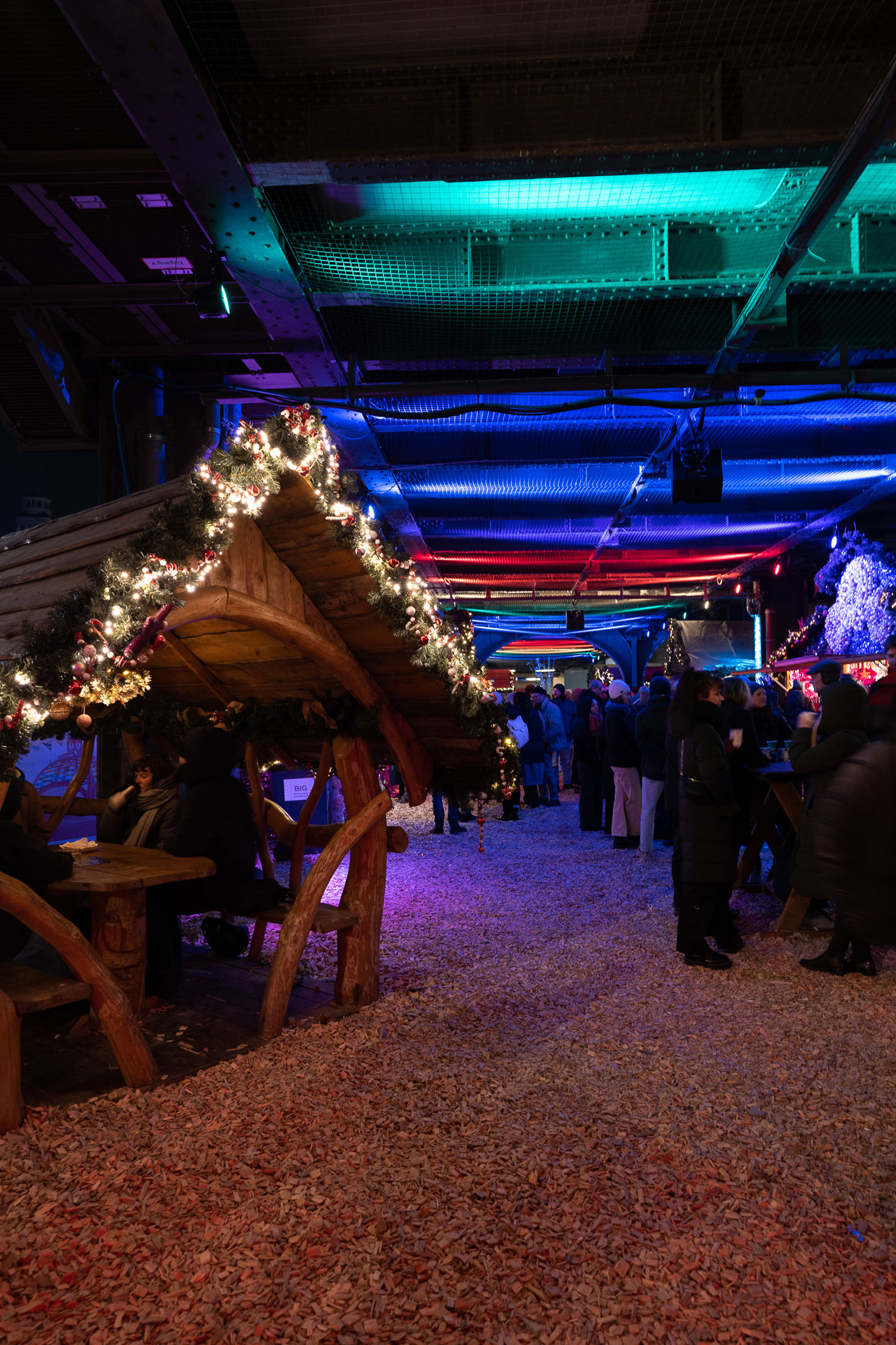 Foto eines Weihnachtsmarktes mit einer geschmückten Holzhütte auf der linken Seite und Menschen im Hintergrund auf der rechten Seite, aufgenommen mit einer Sony Alpha A7C und einem Sony FE 24mm f/1.4 GM