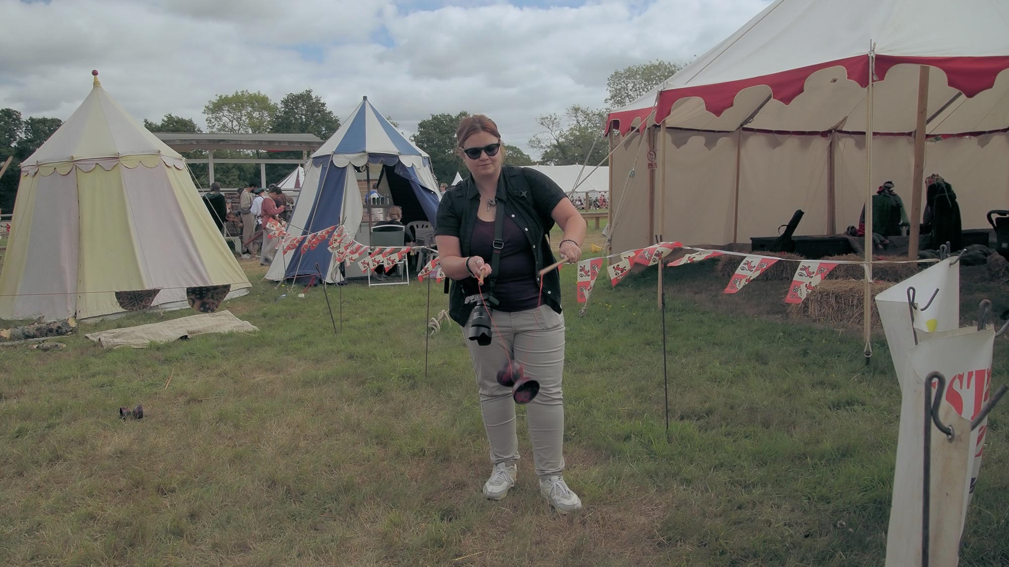 A person attempting a diabolo game at a medieval festival, with bell tents in the background and flags decorating the scene.