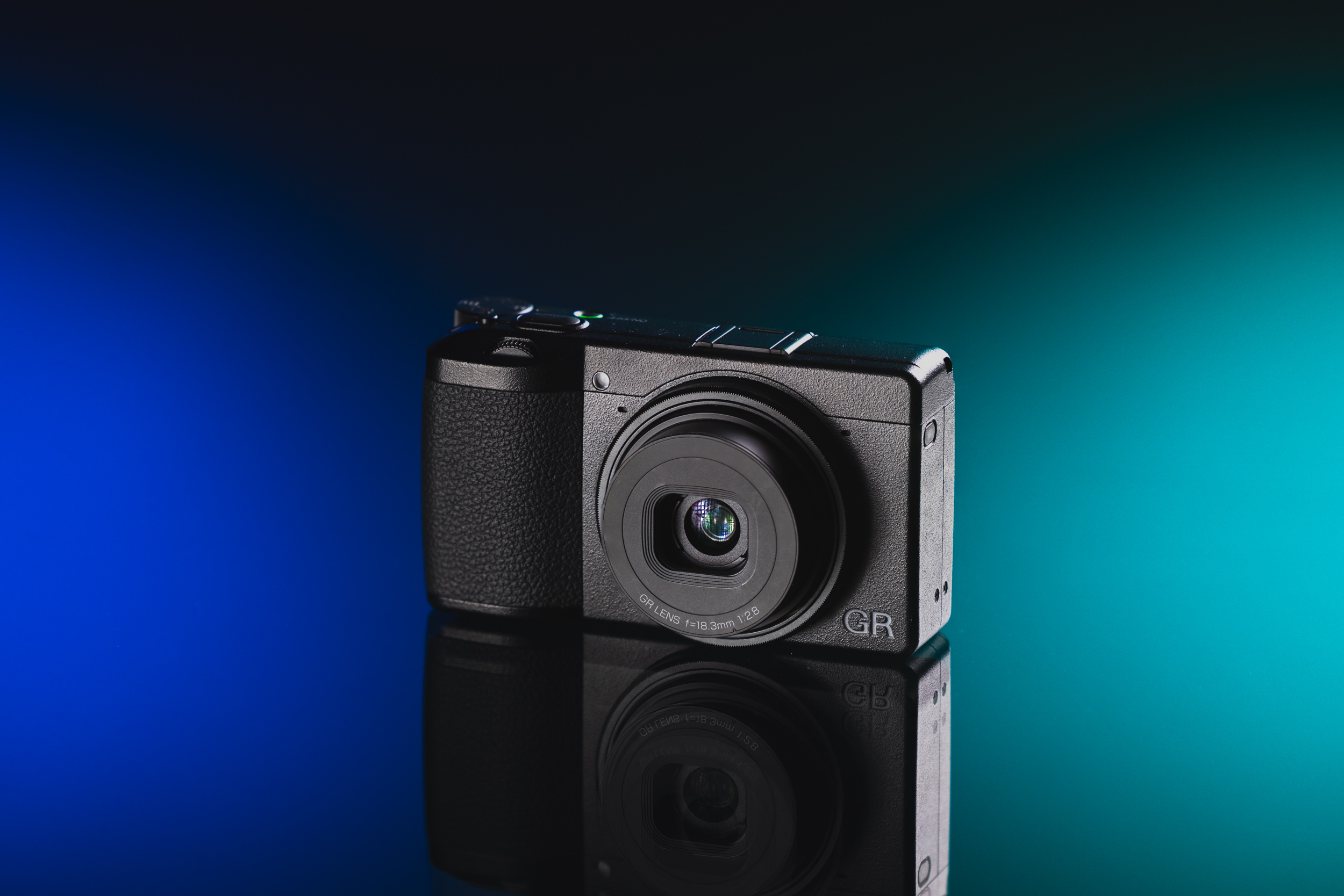 Gebrauchte Ricoh GR III vor einem blau-türkisen Hintergrund
