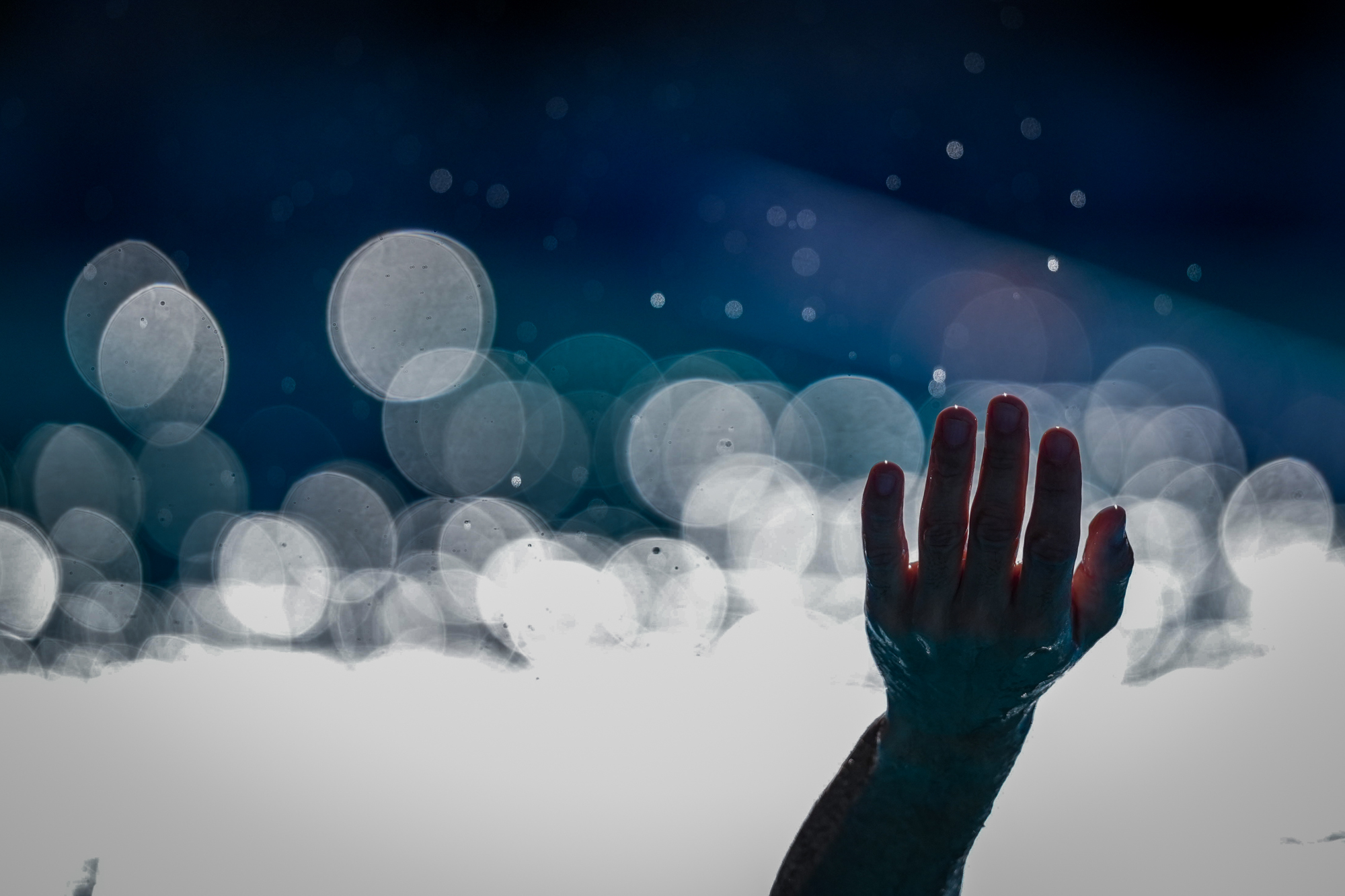 Een uitgestrekte natte hand staat in schril contrast op de voorgrond van een abstract spel met licht dat verschijnt als witte bellen.