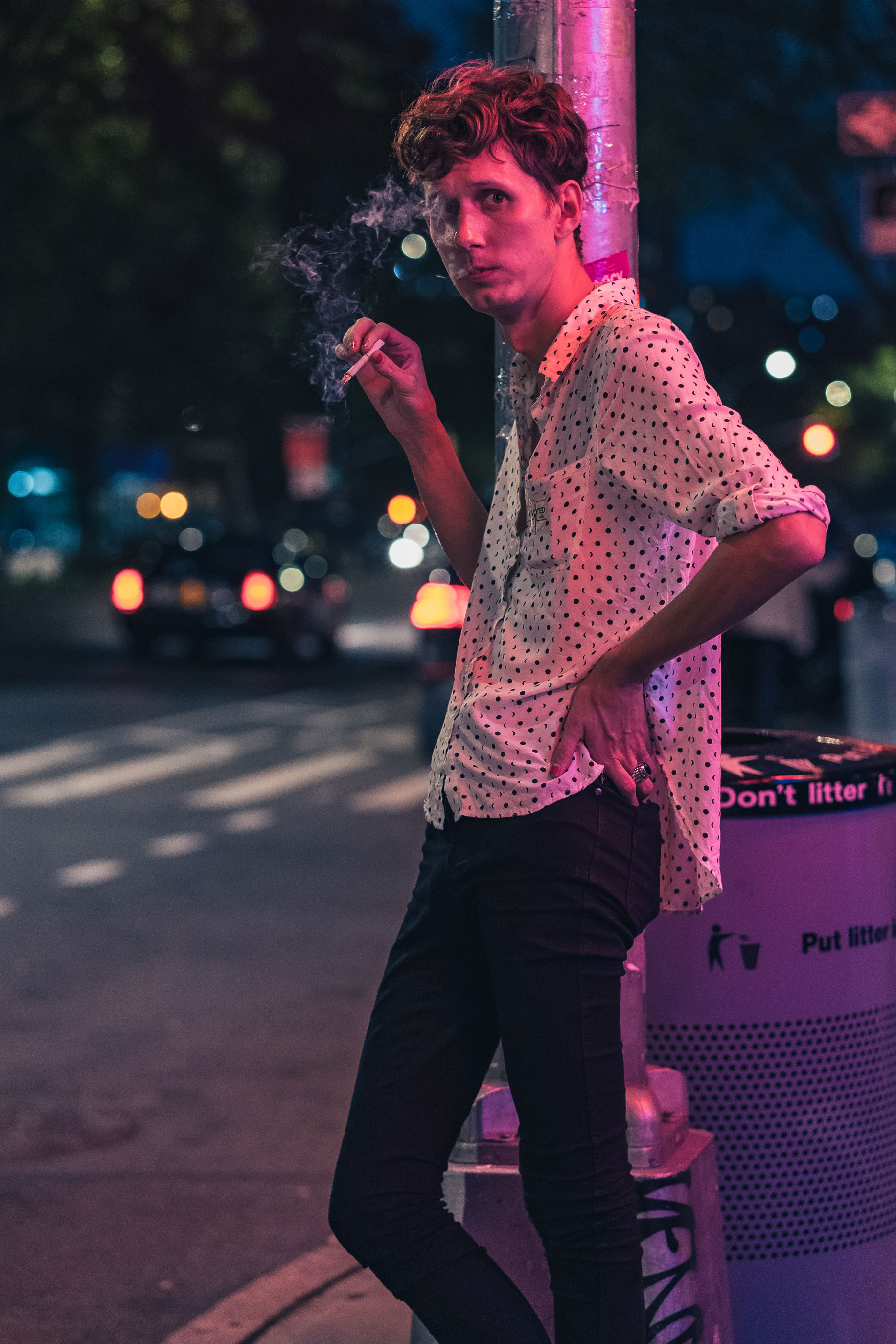Een persoon leunt 's nachts tegen een paal met een wit shirt aan en roze licht op zijn gezicht in New York City, foto gemaakt door Manuel Pena met een Sony A7 III.