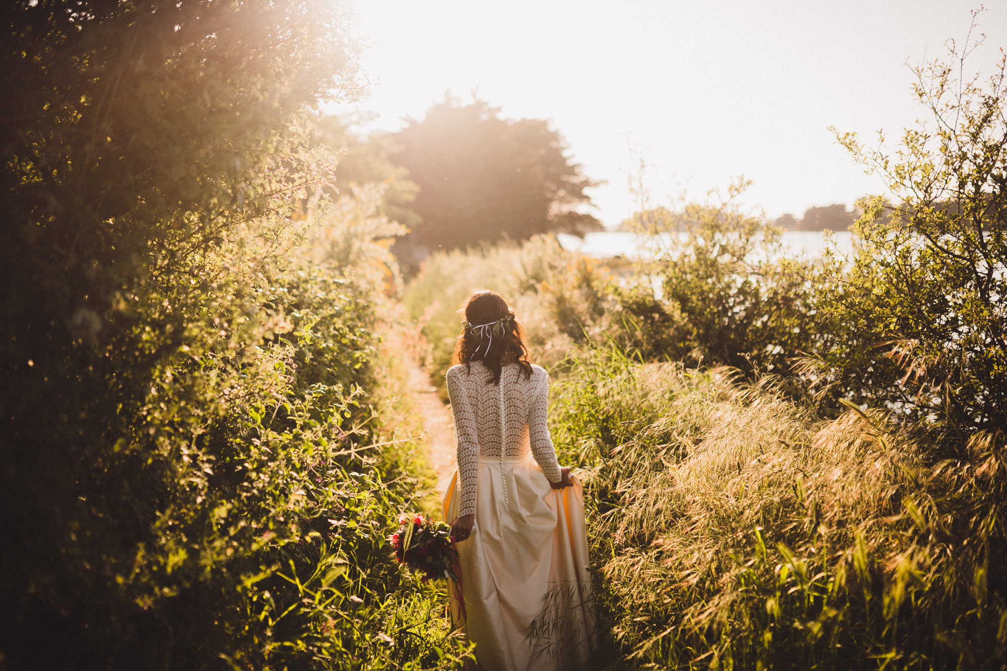 Photo of a woman in a wedding dress, taken from the back. The sun is dazzling.