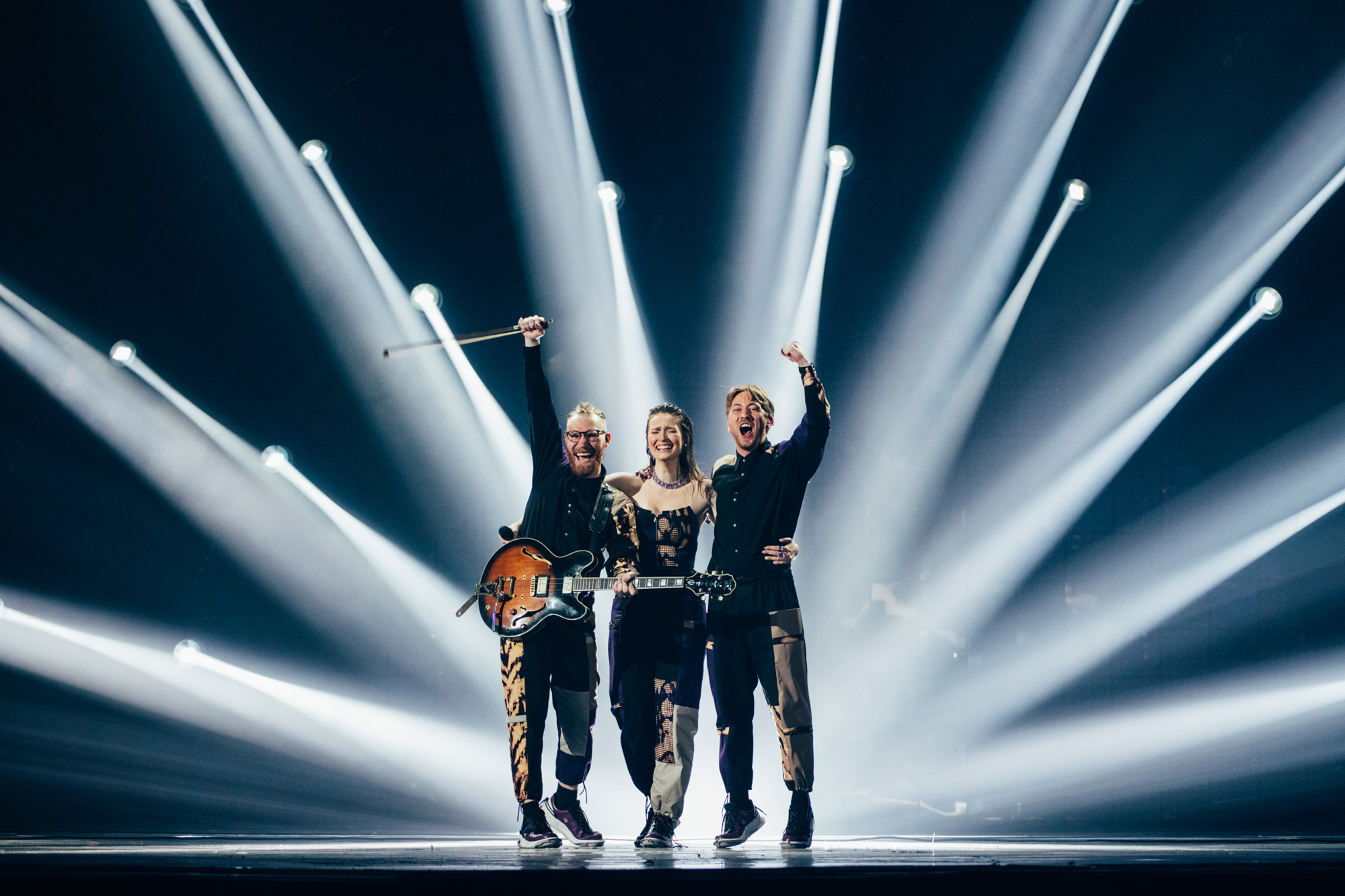 Three performers cheer with their arms raised on stage at Eurovision.