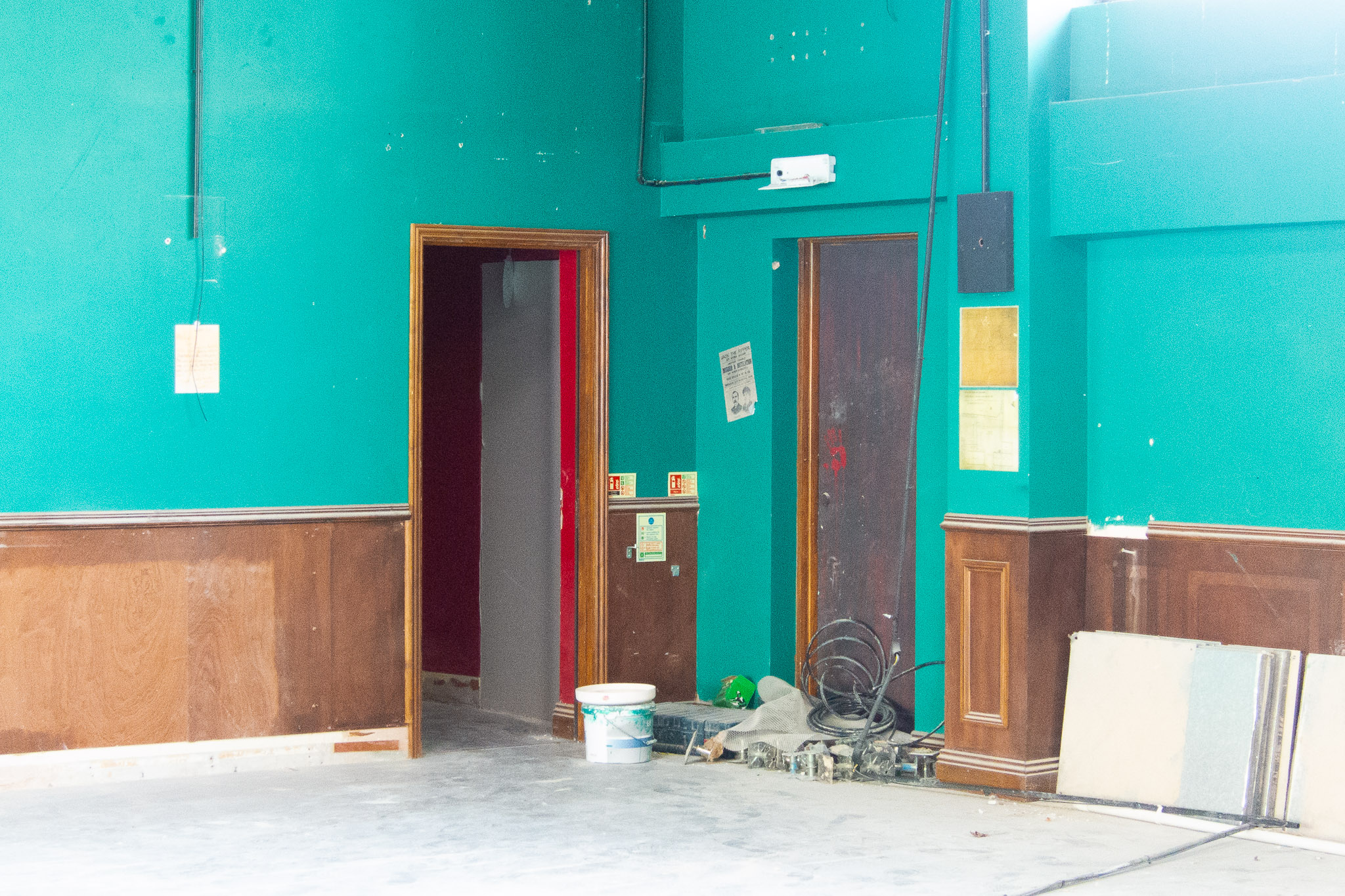 A bright aqua/turquoise wall with two doors in it that appears to be undergoing renovation.