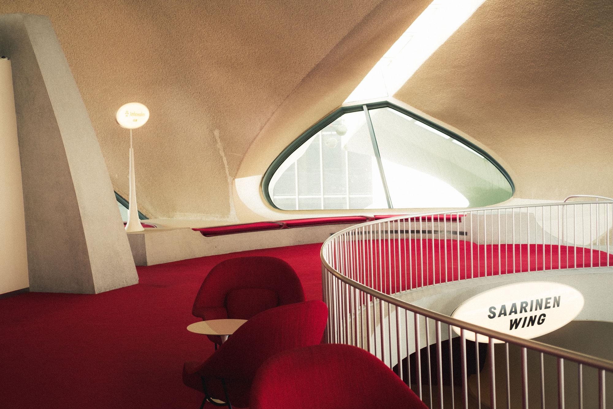 An interior of a hotel, with red carpets and chairs, an oval window and sign saying “Saarinen Wing”, shot by Ian Howorth with a Fujifilm X-Pro 3