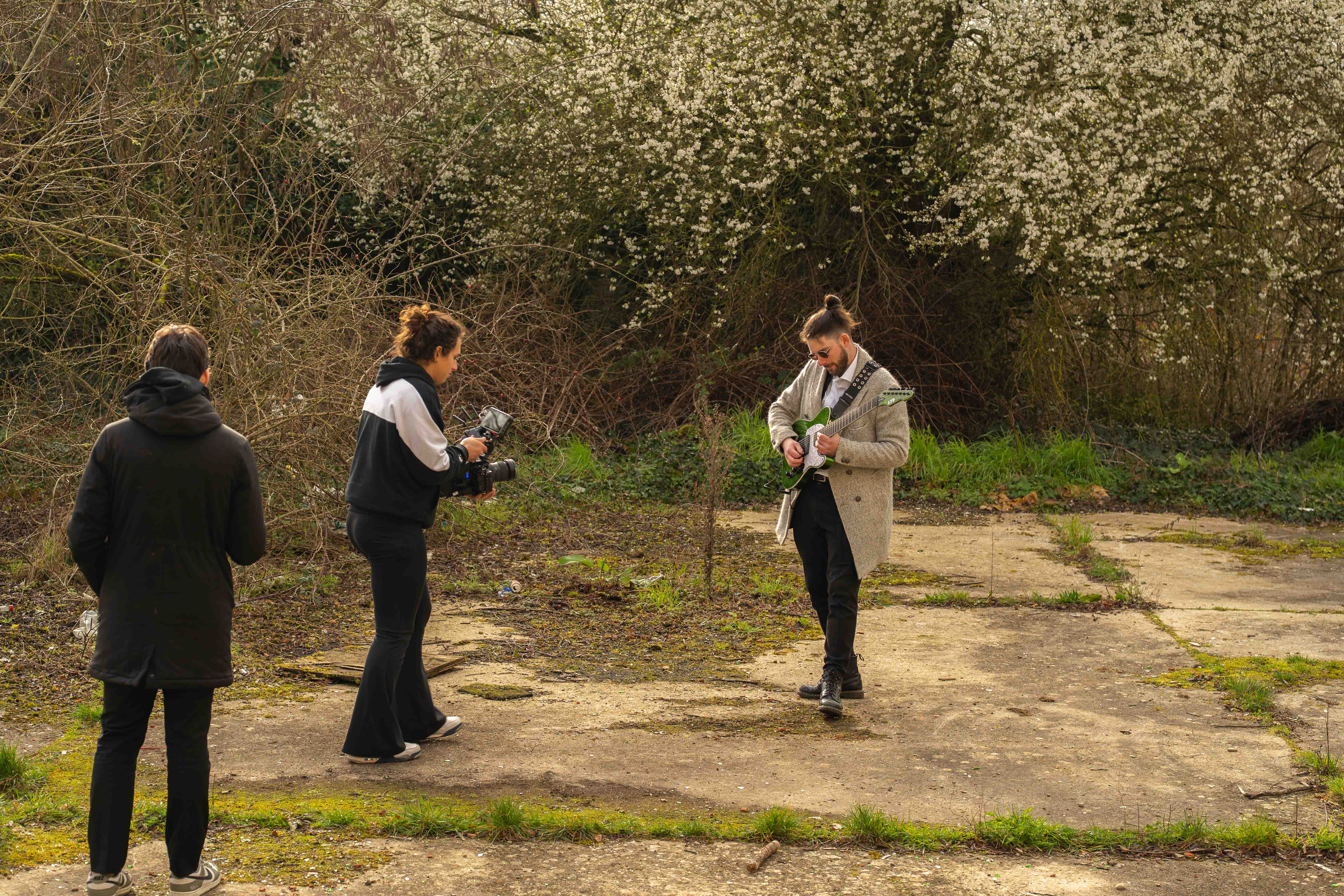 Videographer Lena Hempel films a guitarist playing a green electric guitar outdoors, while another crew member watches from the side. Photo by Lukas Davos. 