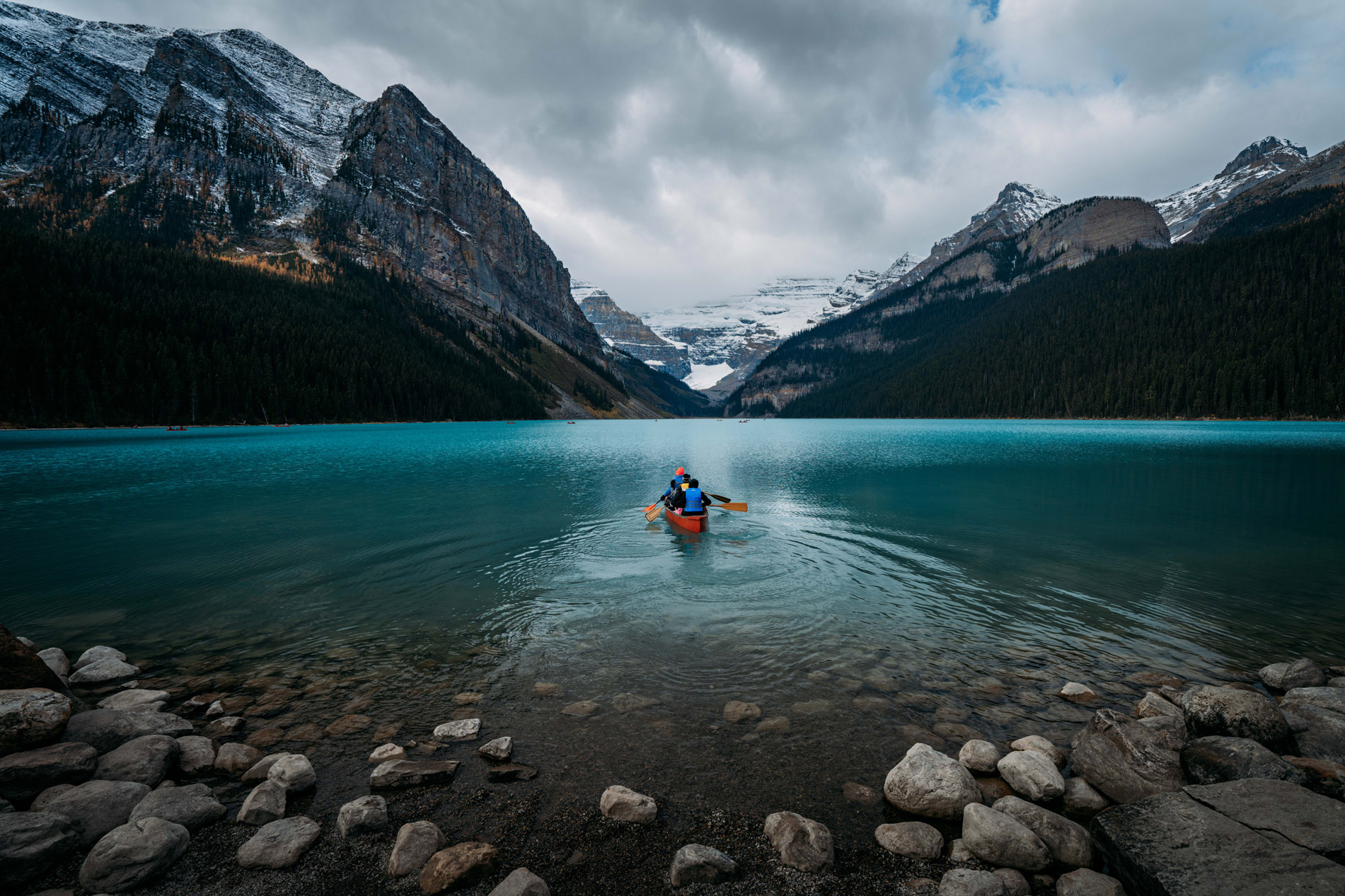 Group of people in red canoe paddling through Lake Louise in Banff National Park, by Jude Allen.