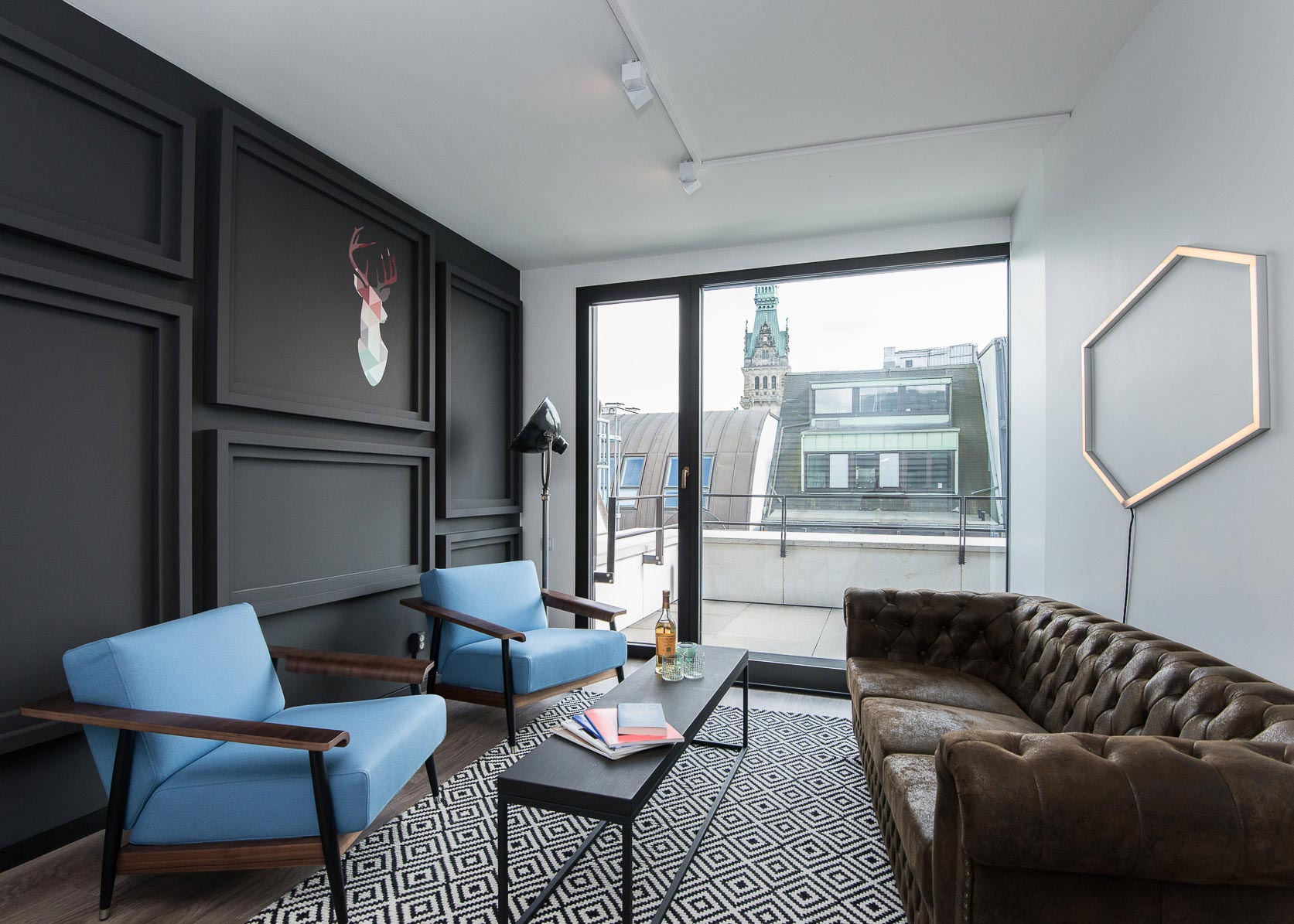 Image d'un salon lumineux avec un mur peint en noir, deux fauteuils bleus, des canapés noirs et un canapé en cuir brun