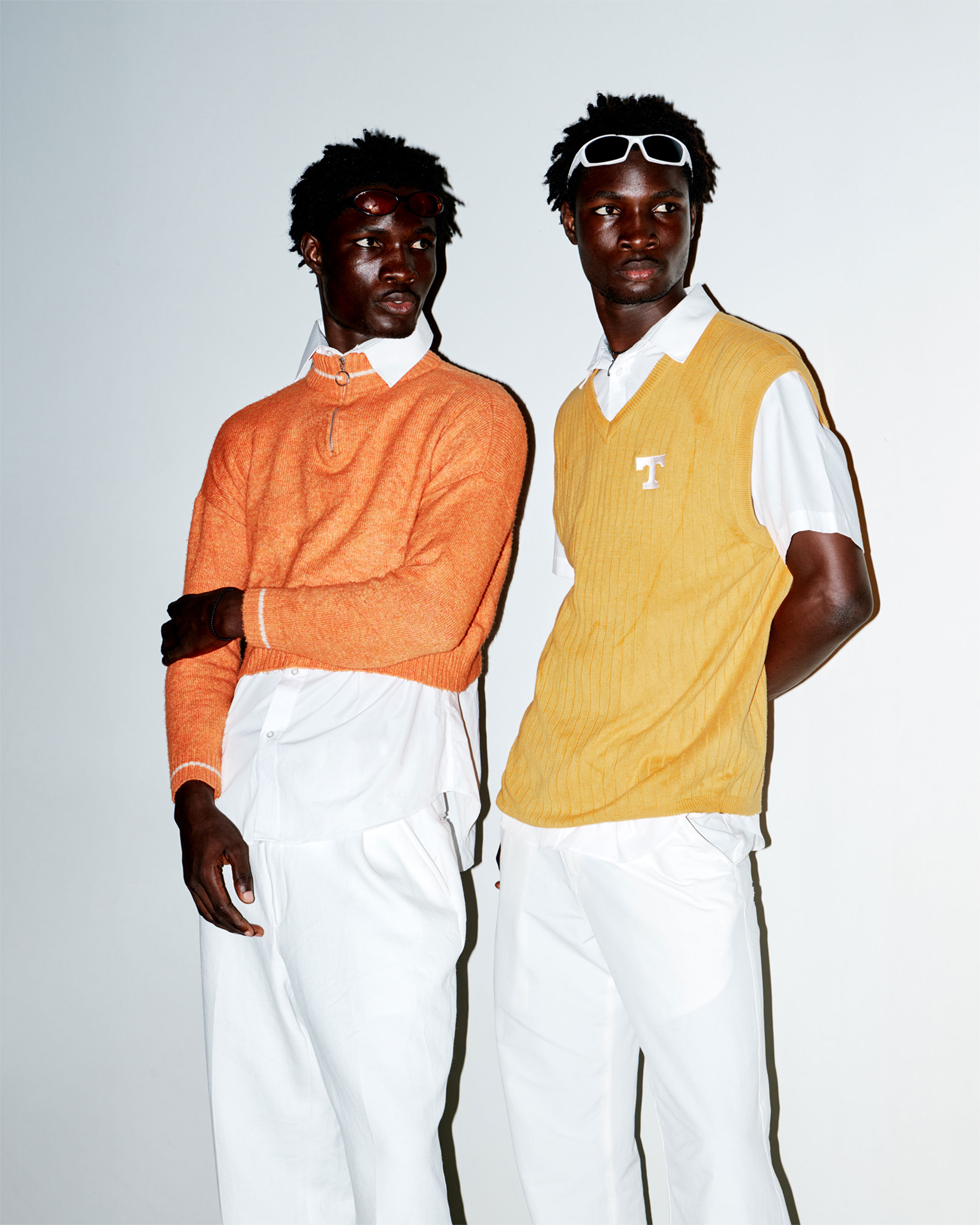 Two Black men standing next to each other and looking to the left, the man on the left with an orange top, on the right with a yellow top, shot by Lisa Marie Asubonteng