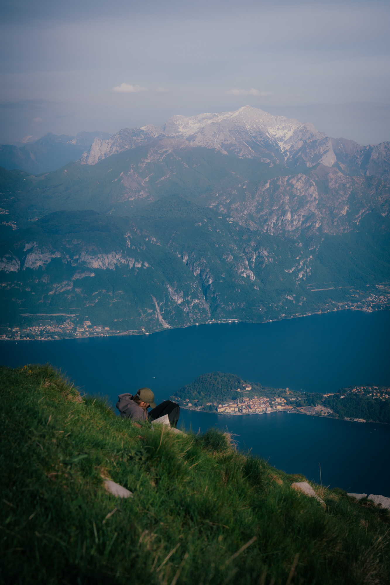 Person sitting on a grassy slope with a view of the mountains and Lake Como