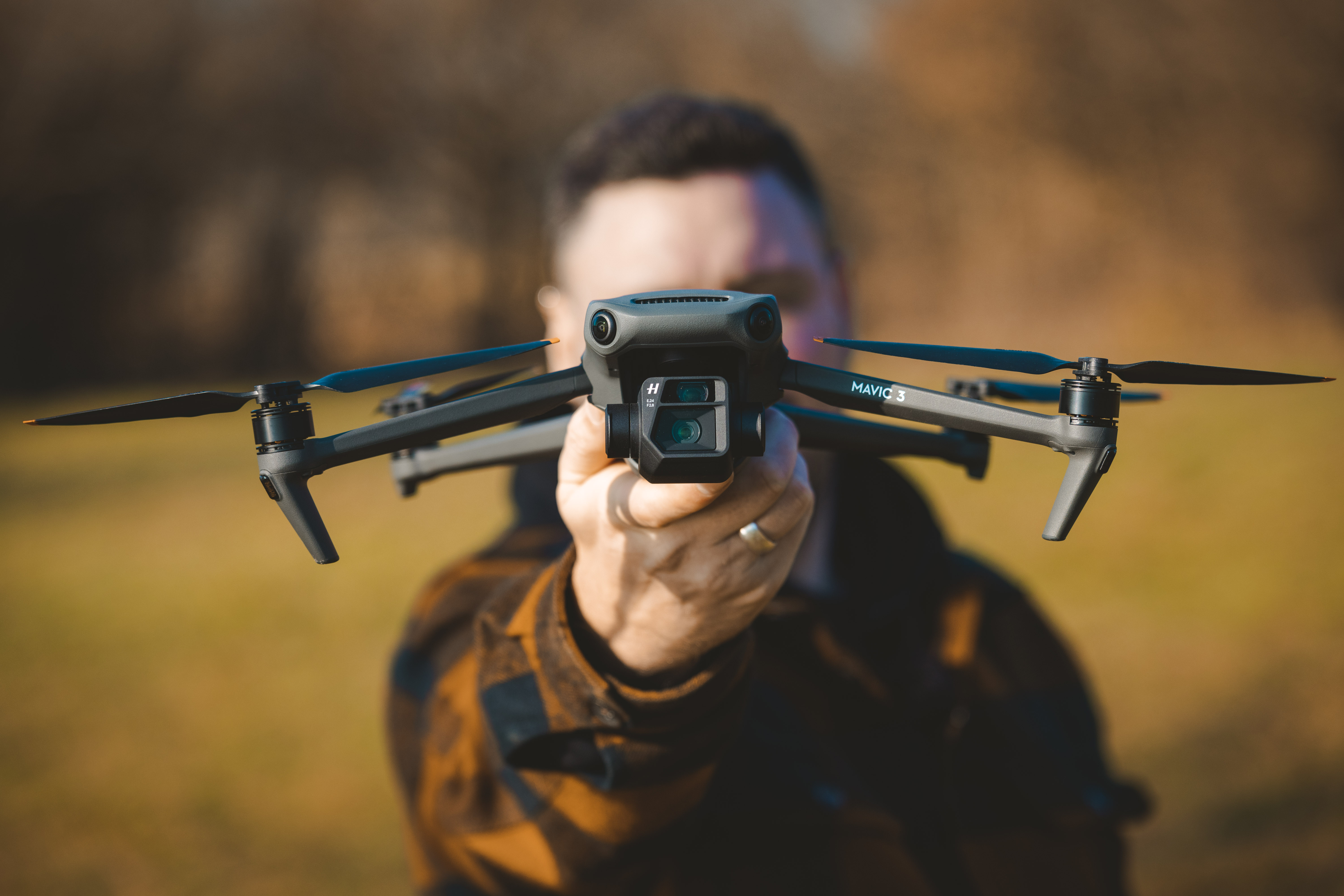 DJI Mavic 3 drone held out towards the camera, showing the front dual camera system and folded arms outdoors.