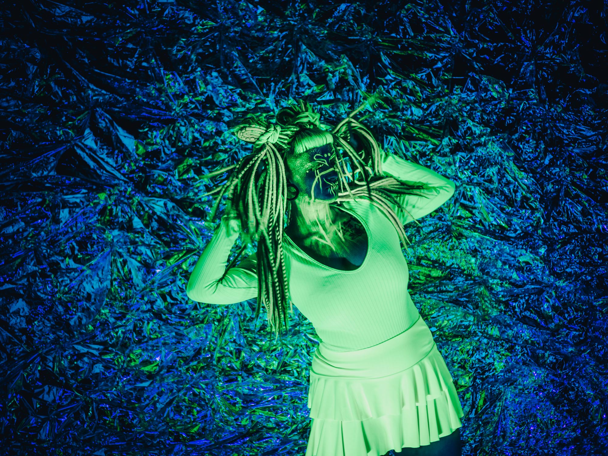 A model lying on grass with a green UV effect against a blue background, shot by Emily Lowrey with the Panasonic Lumix DC-GH6.