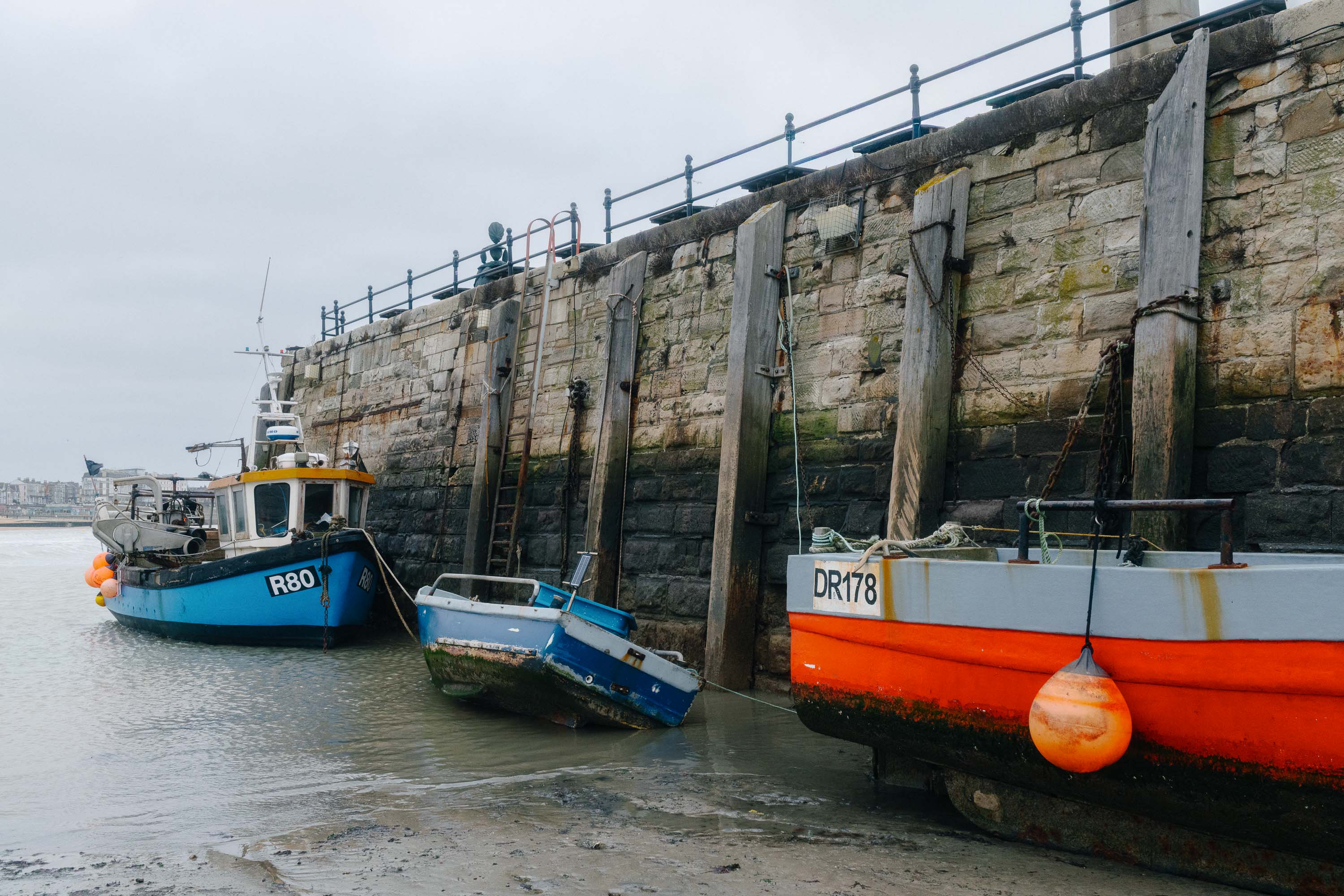 Fischerboote, die bei Ebbe an einer steinernen Hafenmauer liegen. Aufgenommen von Connor Redmond mit einer Sony RX1R III.