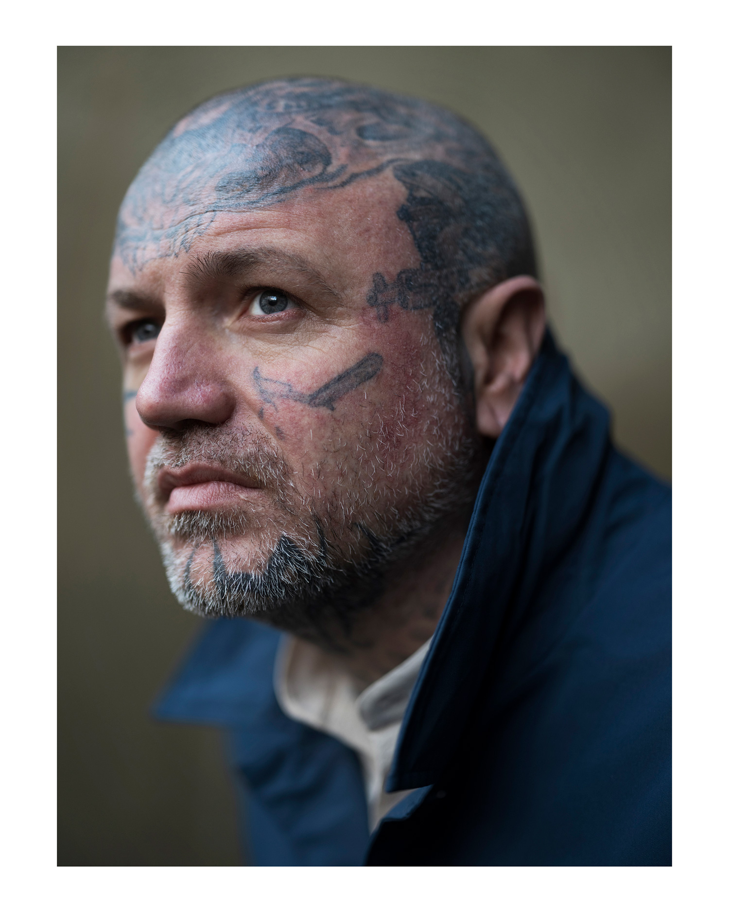 A close-up of a tattooed model wearing a blue coat standing in front of a wall, photo by Simon Murphy with the Fujifilm GFX 100.