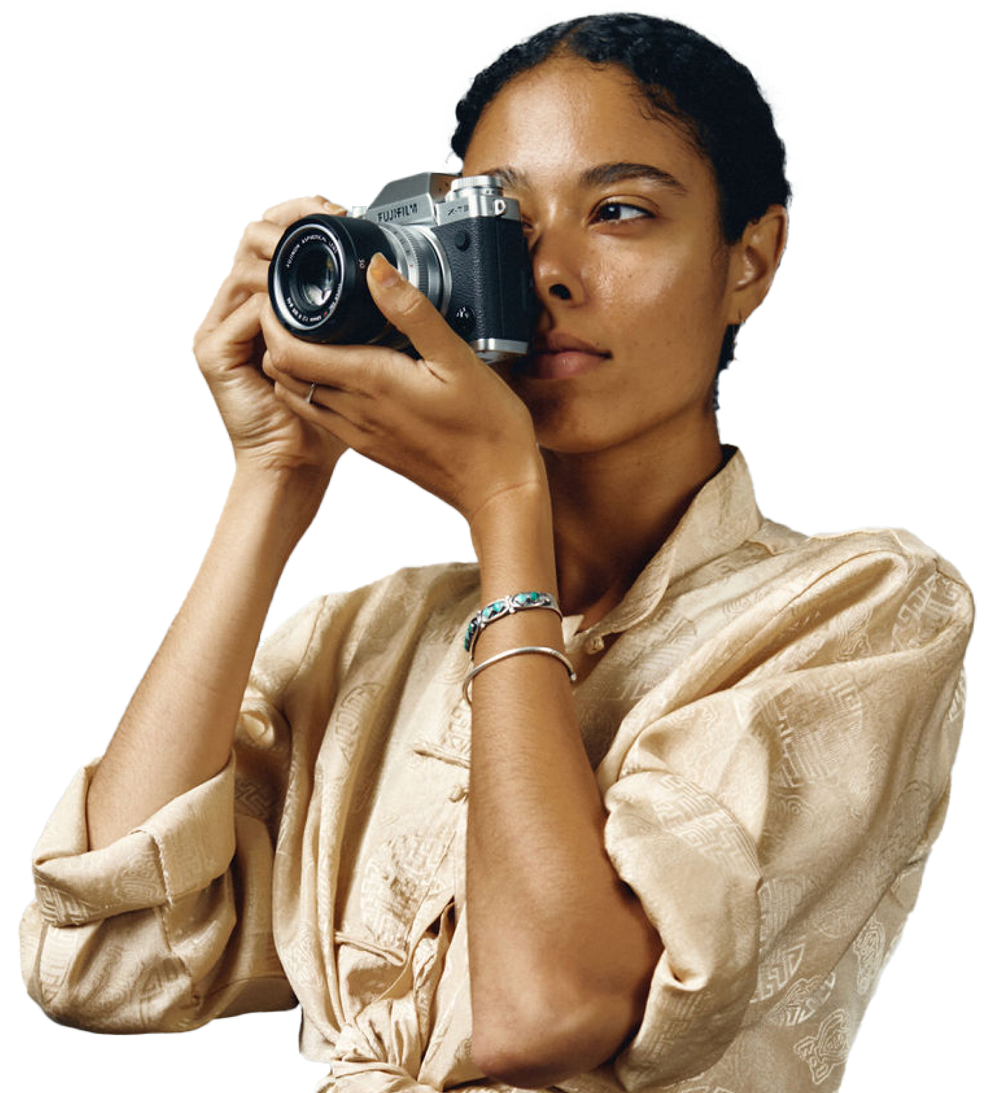 Eine Person in einem cremefarbenen Seidenhemd, die ein Foto mit einer spiegellosen Fujifilm-Kamera macht