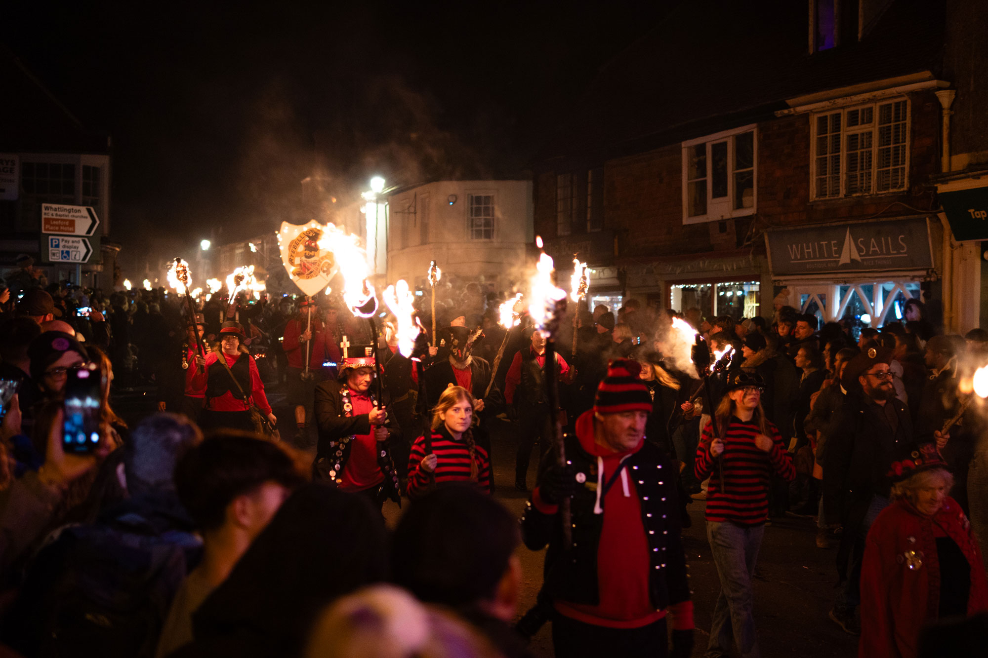 Ein Fackelumzug, der nachts durch eine Straße zieht. Die Menschen sind in Schwarz-Rot gekleidet und einige halten Fackeln in der Hand.
