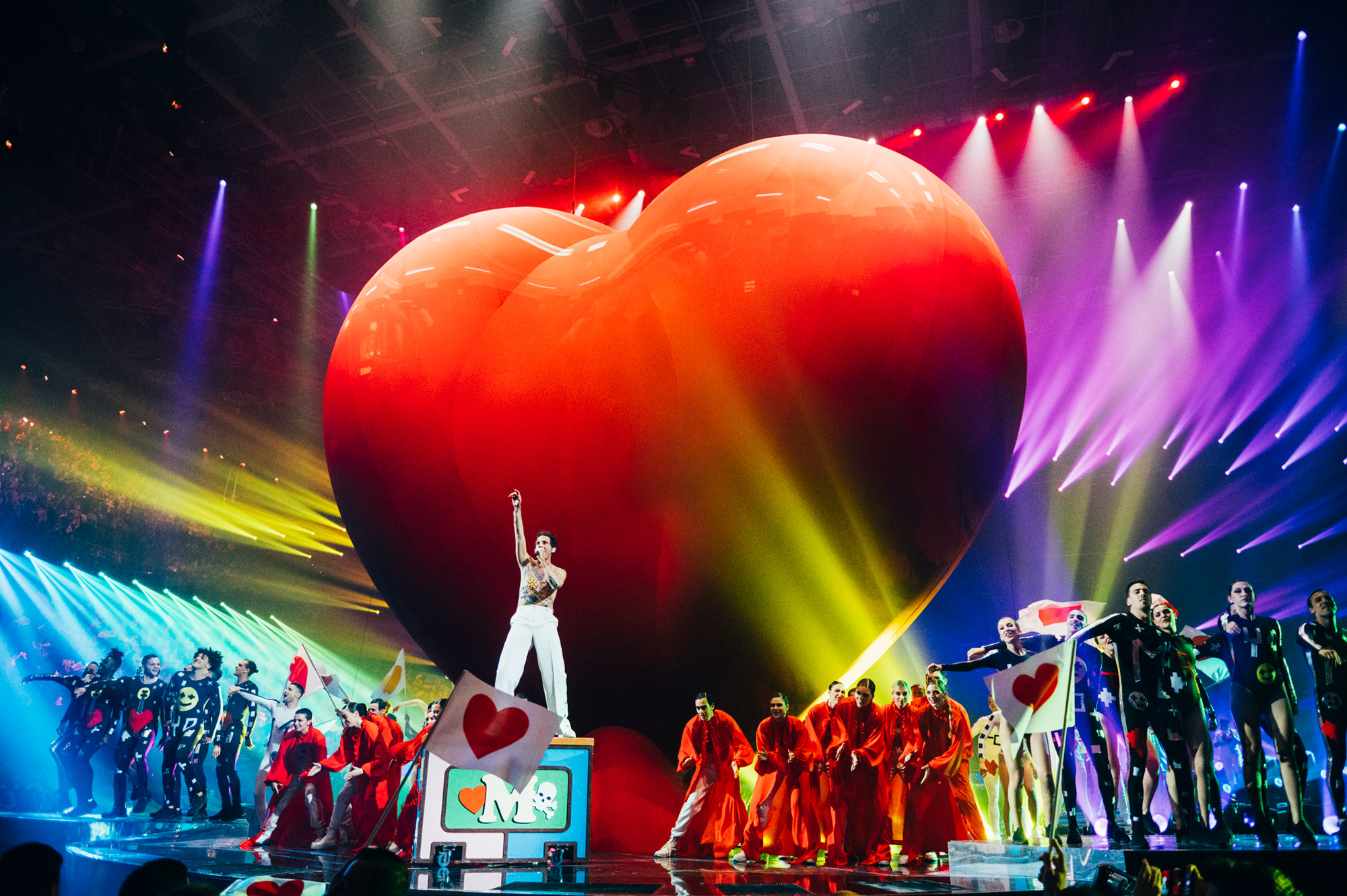 Mika at Eurovision in front of a large red heart.