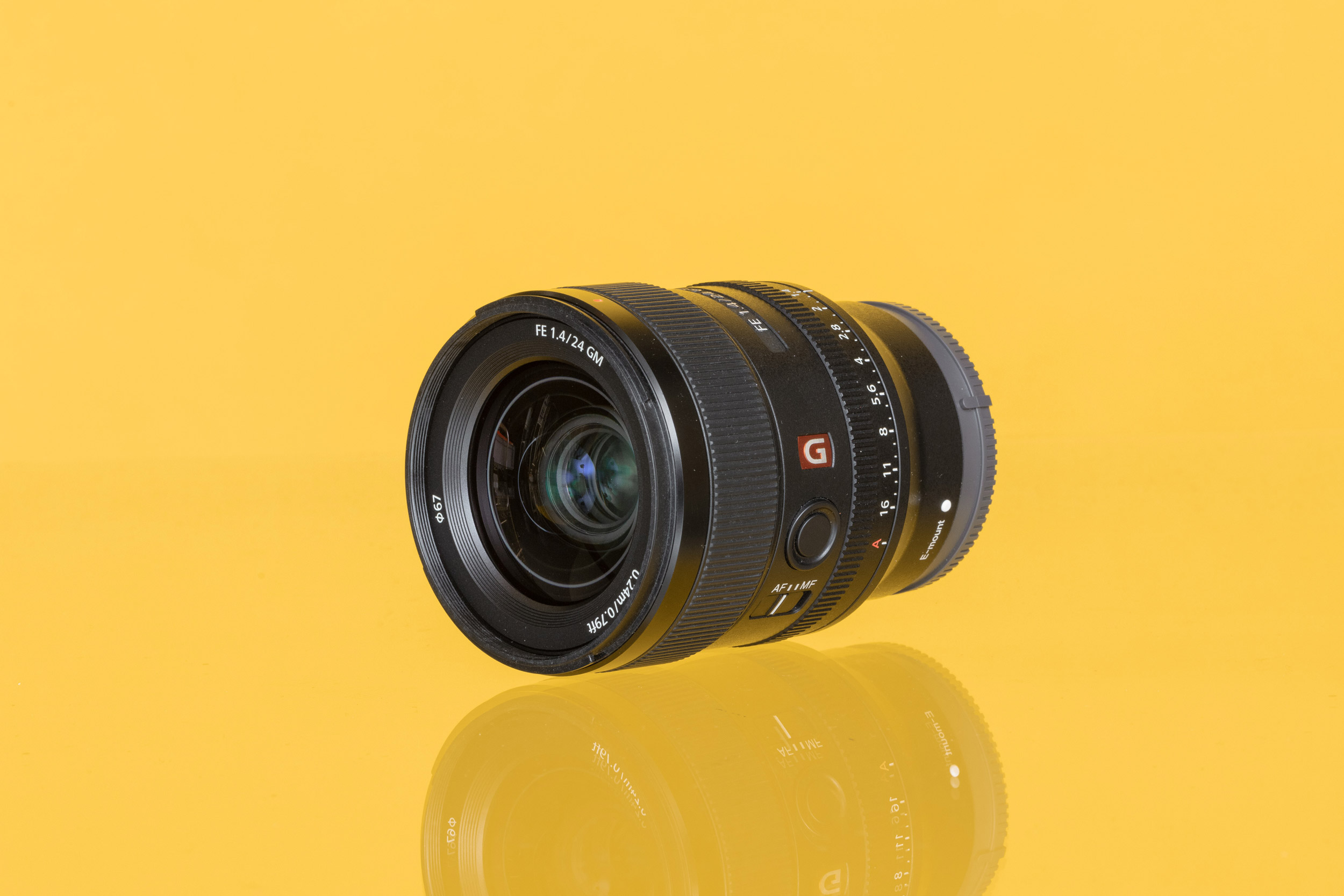 A photo of a Sony FE 24mm f/1.4 GM wide-angle prime lens against a yellow background