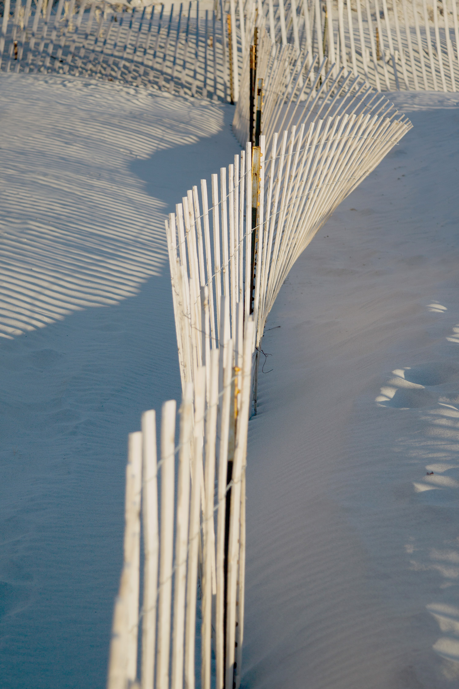 Ein Holzzaun am Strand, im Sonnenlicht und im Schatten. Aufgenommen von Kim Fuller.