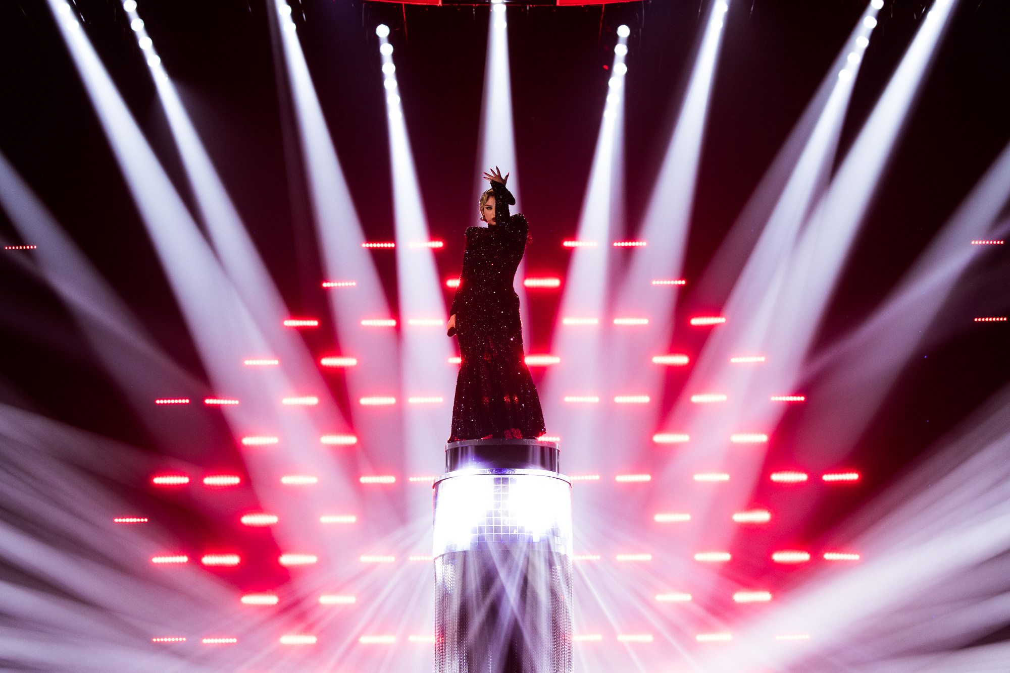 Künstler:in auf der Bühne beim ESC 2023, mit Scheinwerfern, die auf die Person gerichtet sind, und roten Lichtern dahinter auf der Bühne, aufgenommen von Corinne Cumming mit der Canon EOS R5.