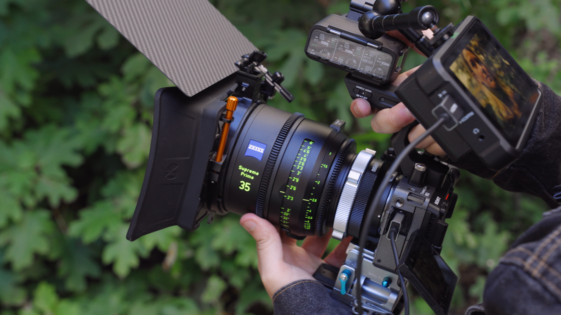 Person hand-holding Sony Fx3 camera in front of green bush with monitor on top
