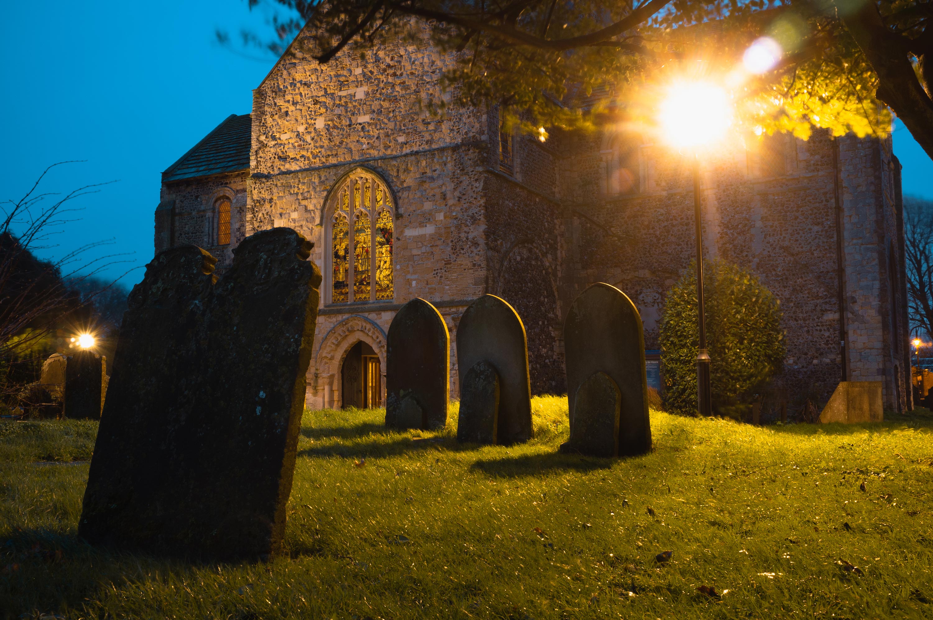 A graveyard and church at dusk, illuminated by a street light, photo by Jakub Golis with a Fujifilm X100