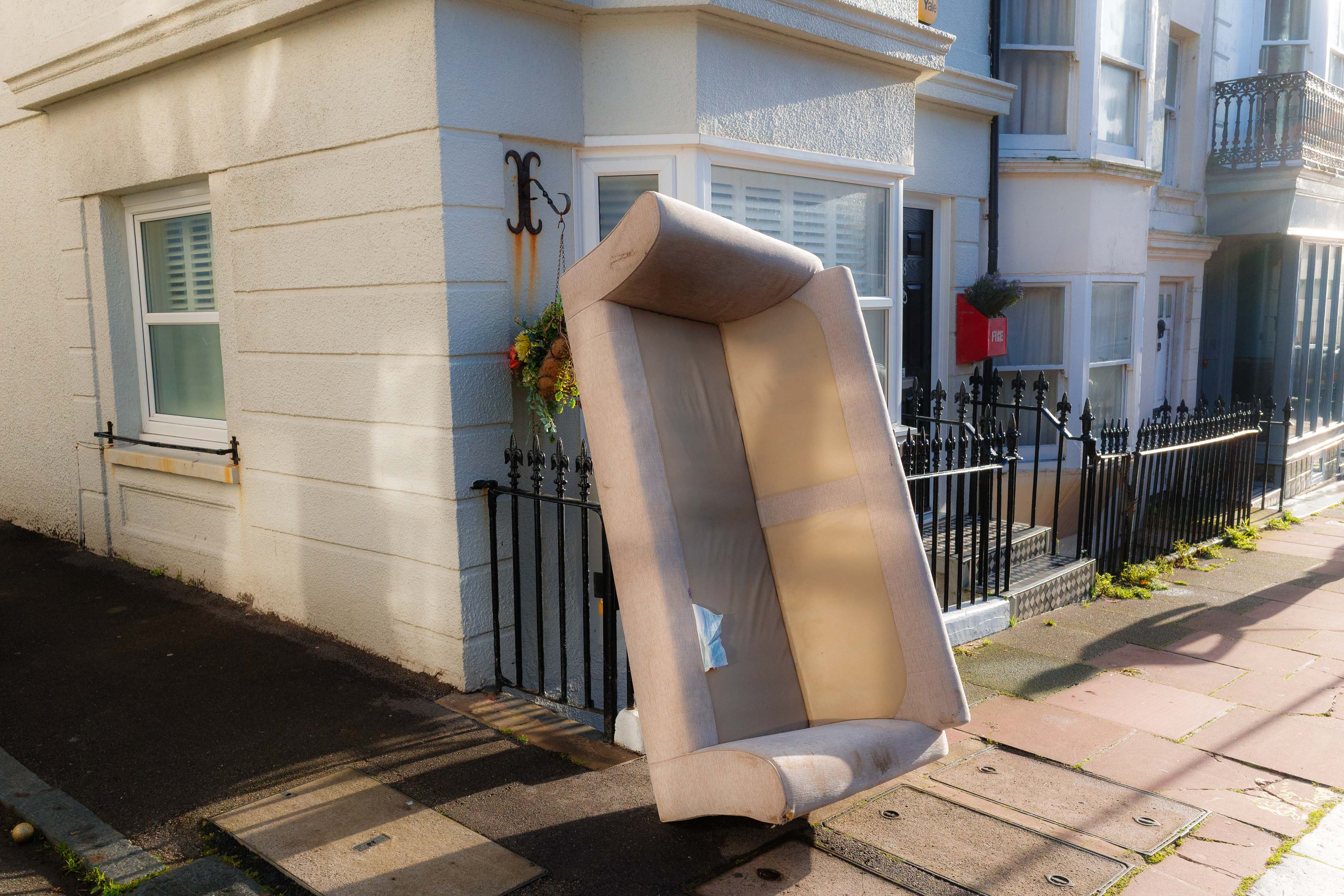 Spontane Streetaufnahme eines weggeworfenen Sofas, das in der sanften Wintersonne an einem Geländer vor einem Wohngebäude lehnt. Aufgenommen mit einer Ricoh GR IV.