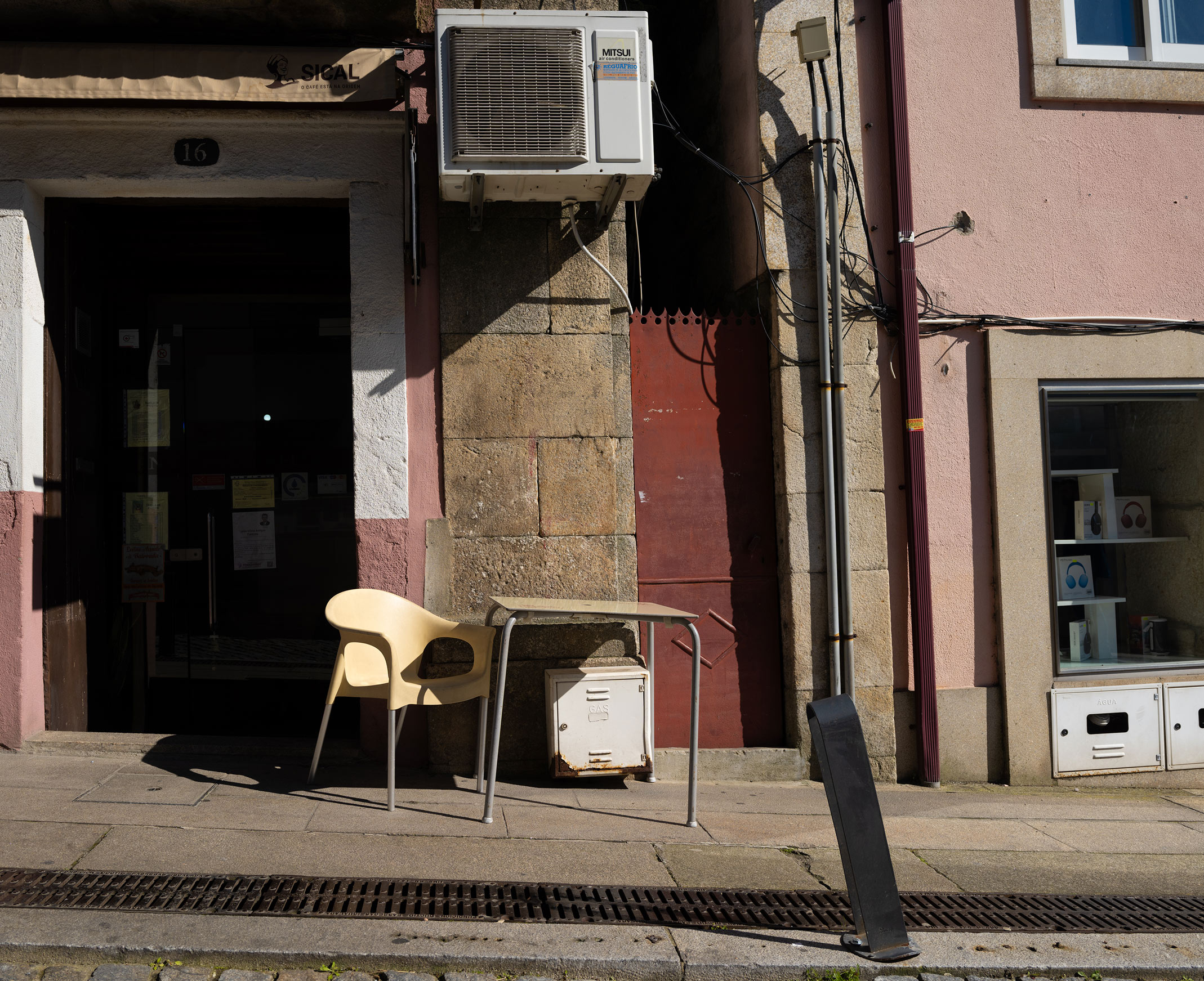 An empty chair and small table on the pavement outside an open doorway. Shot on the Fujifilm GFX100RF by Amy Moore.