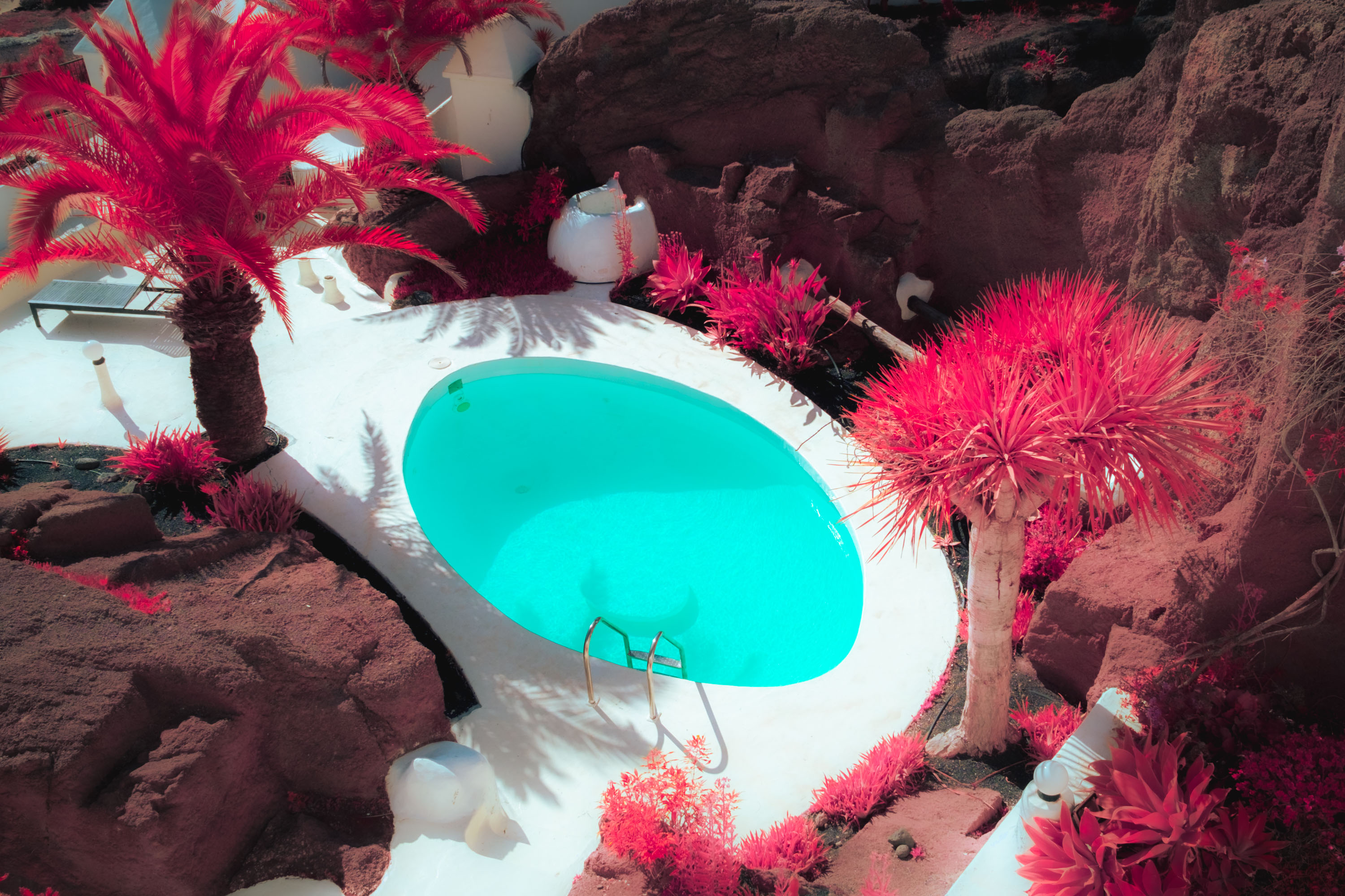 An infrared photo of a bright blue swimming pool surrounded by trees in Lanzarote, shot by Ian Howorth with an IR-Converted Fujifilm X-T1

