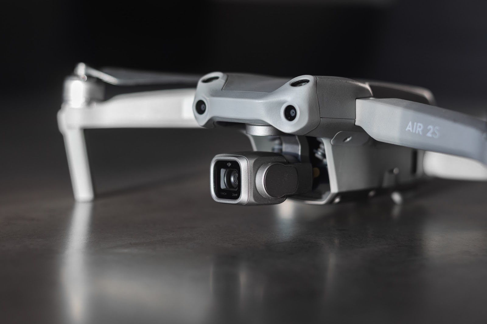 A photo focussing on the lens of an unfolded DJI Mavic Air 2S drone, sat on a grey floor as a background 